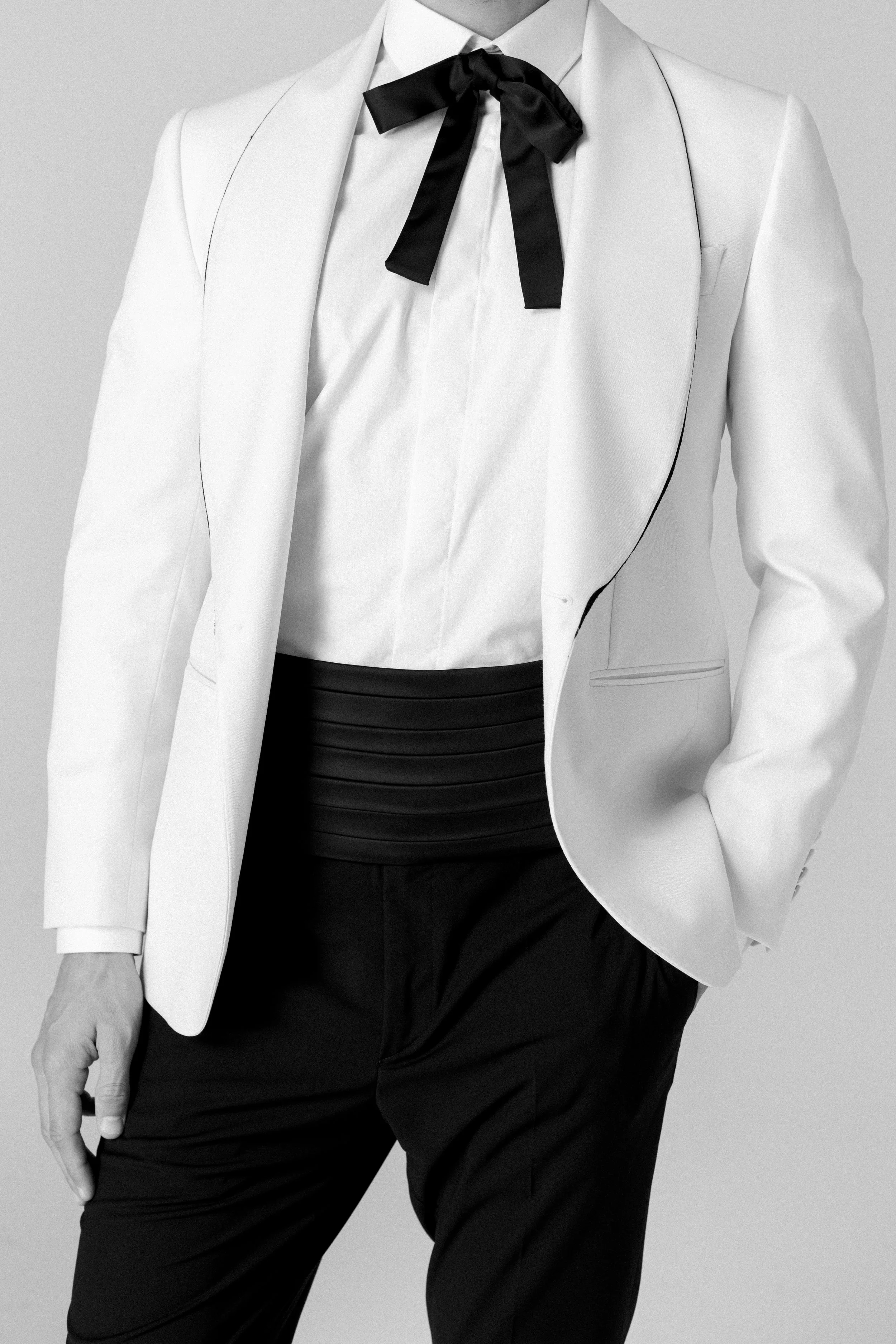 Una persona indossa un abito elegante bianco, con una cravatta nera a fiocco e pantaloni neri, in stile sofisticato.