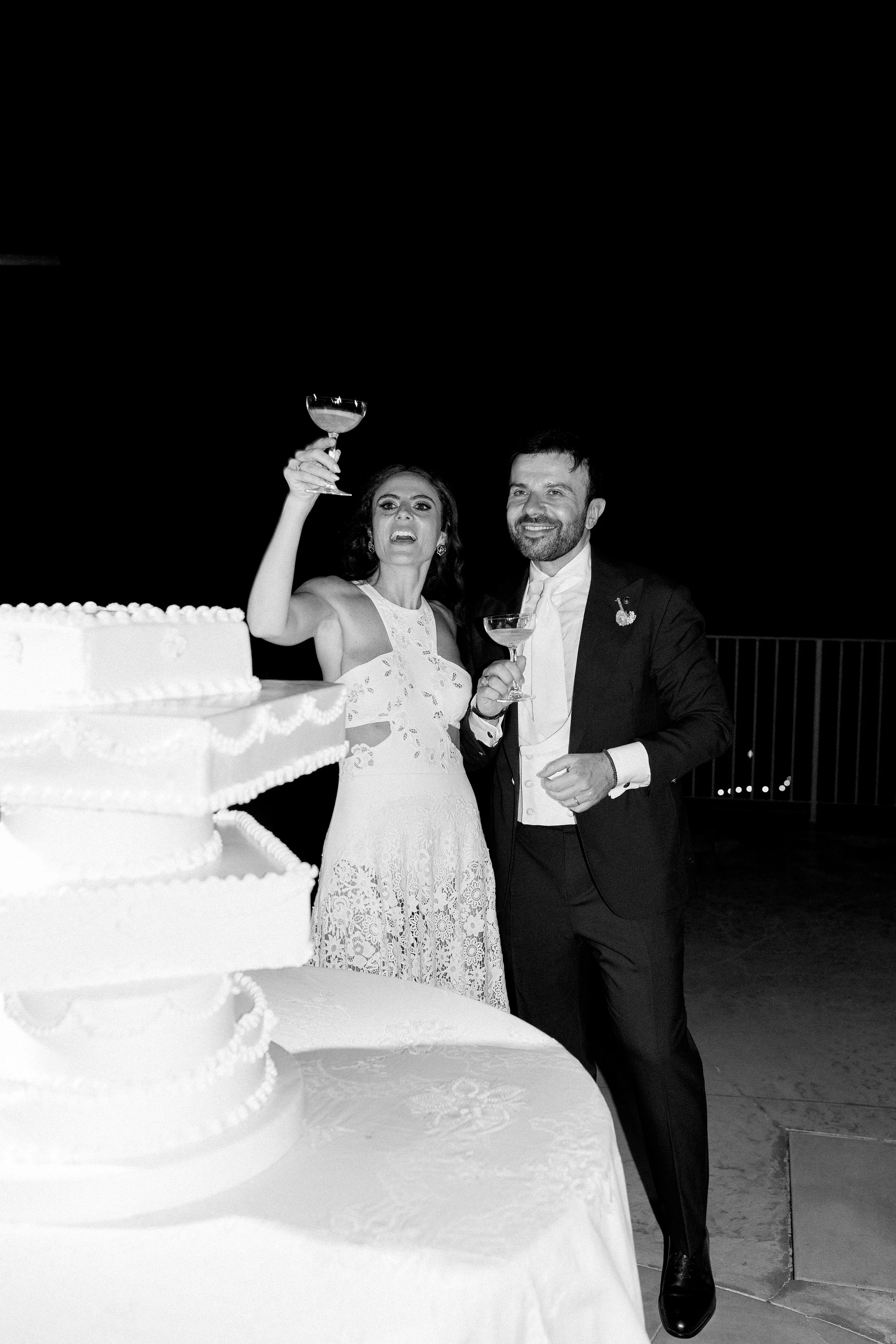 Una coppia di sposi che festeggia con un brindisi di fronte a una torta di matrimonio, al buio.