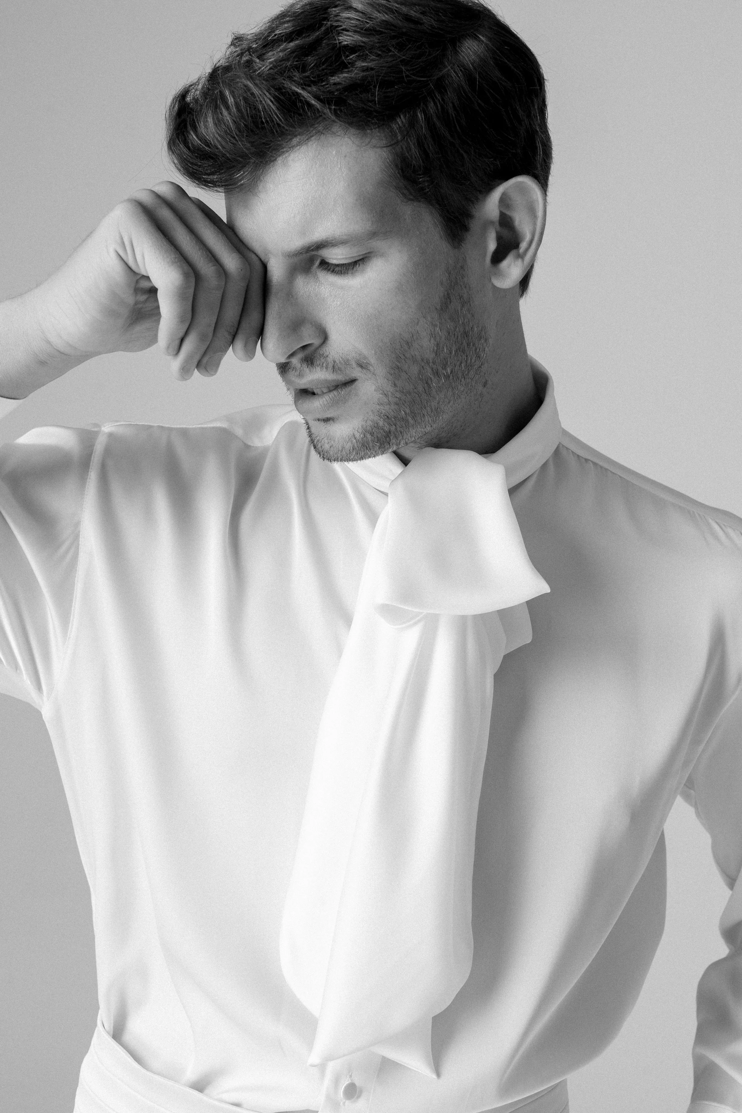 Ritratto di un uomo con abbigliamento elegante, toccandosi la fronte in un gesto pensieroso, in bianco e nero.