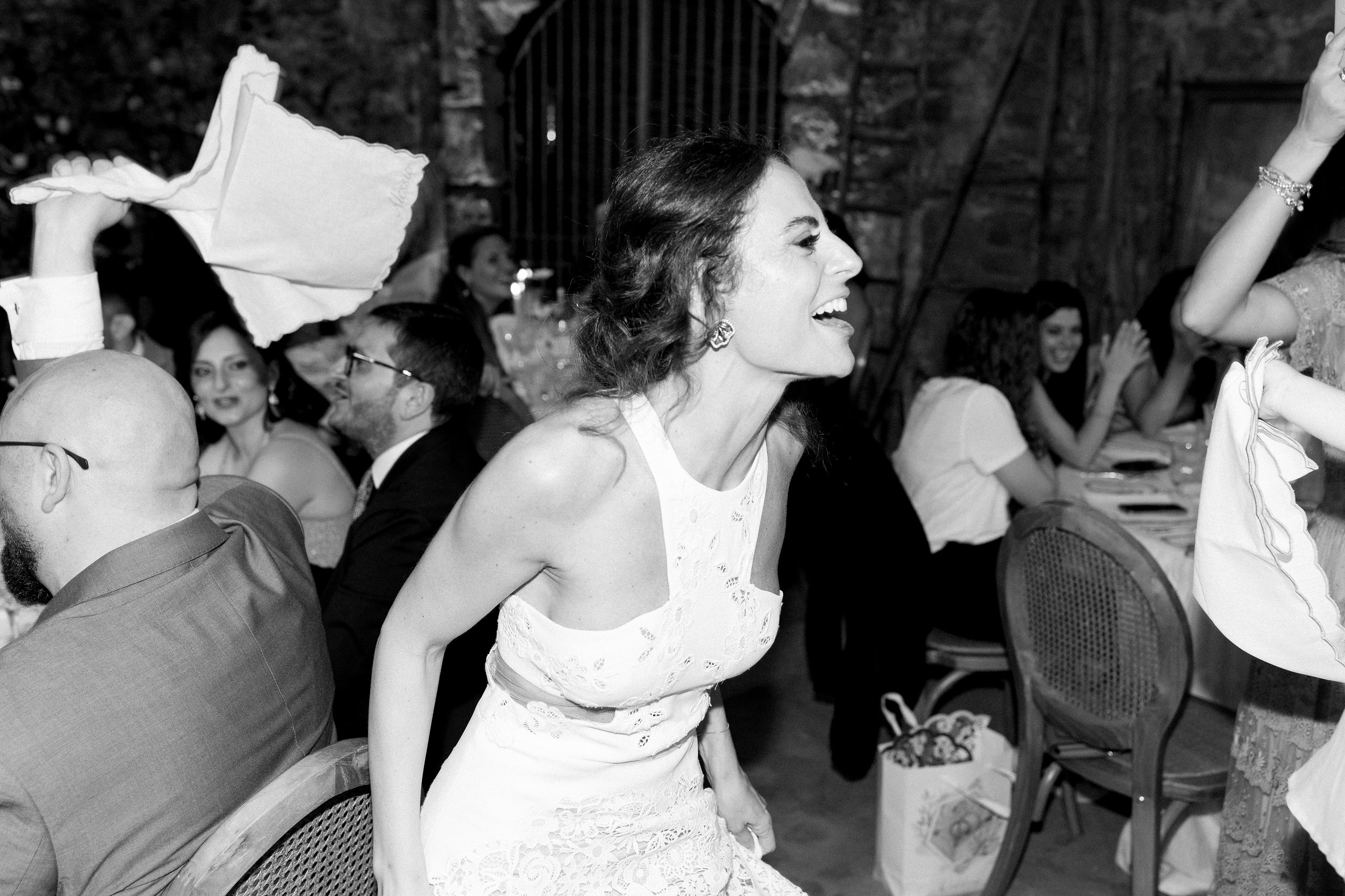 Donna che sorride tra un gruppo di persone sedute a un tavolo durante un evento sociale o feste, in un ambiente elegante.