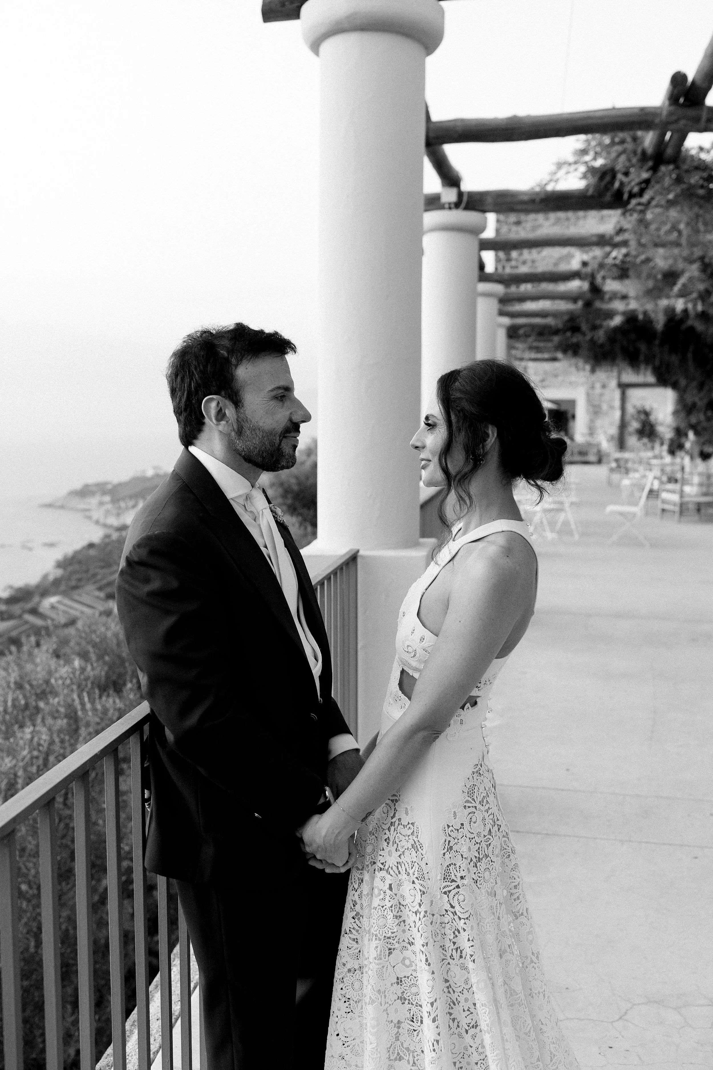 Una coppia sorriso, agli inizi di un matrimonio, si tengono per mano, con il mare sullo sfondo, in un ambiente all'aperto.