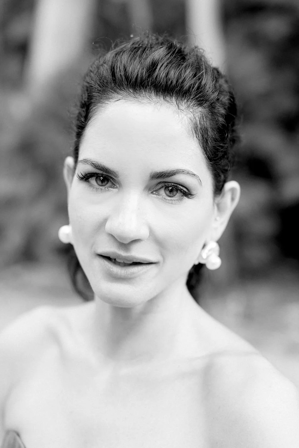 Ritratto in bianco e nero di una donna con trucco raffinato, orecchini vistosi e capelli acconciati, con sfondo sfocato