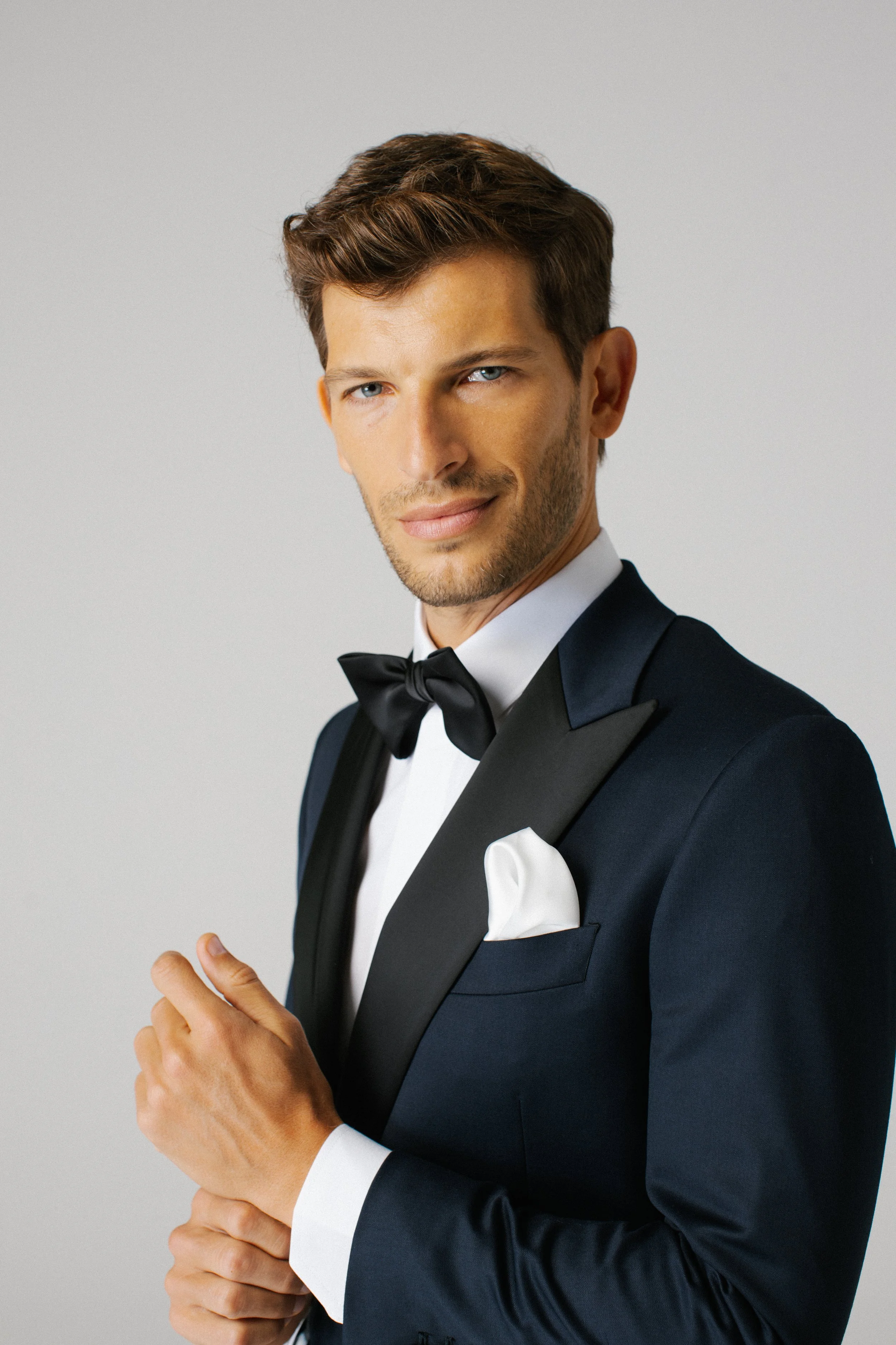 Uomo elegante in abito da sera con papillon nero e pochette bianca che sorride.