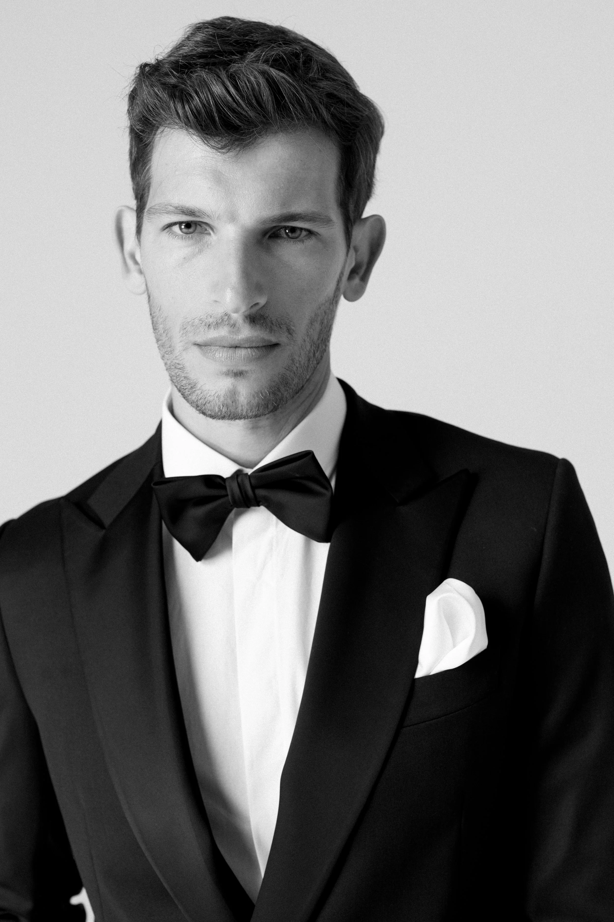 Un uomo elegante in abito da smoking nero con papillon, camicia bianca e pochette bianca, in uno scatto in bianco e nero.