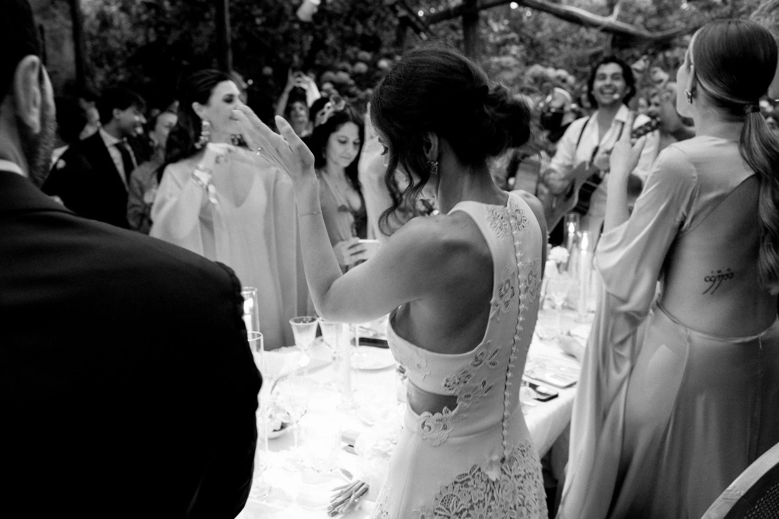 Una donna in abito da sposa invita gli ospiti a ballare durante un matrimonio all'aperto.