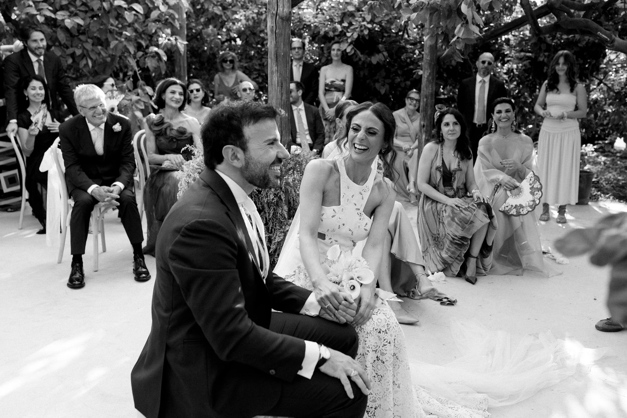 Momento di un matrimonio con la coppia seduta e gli ospiti sorridenti sullo sfondo.