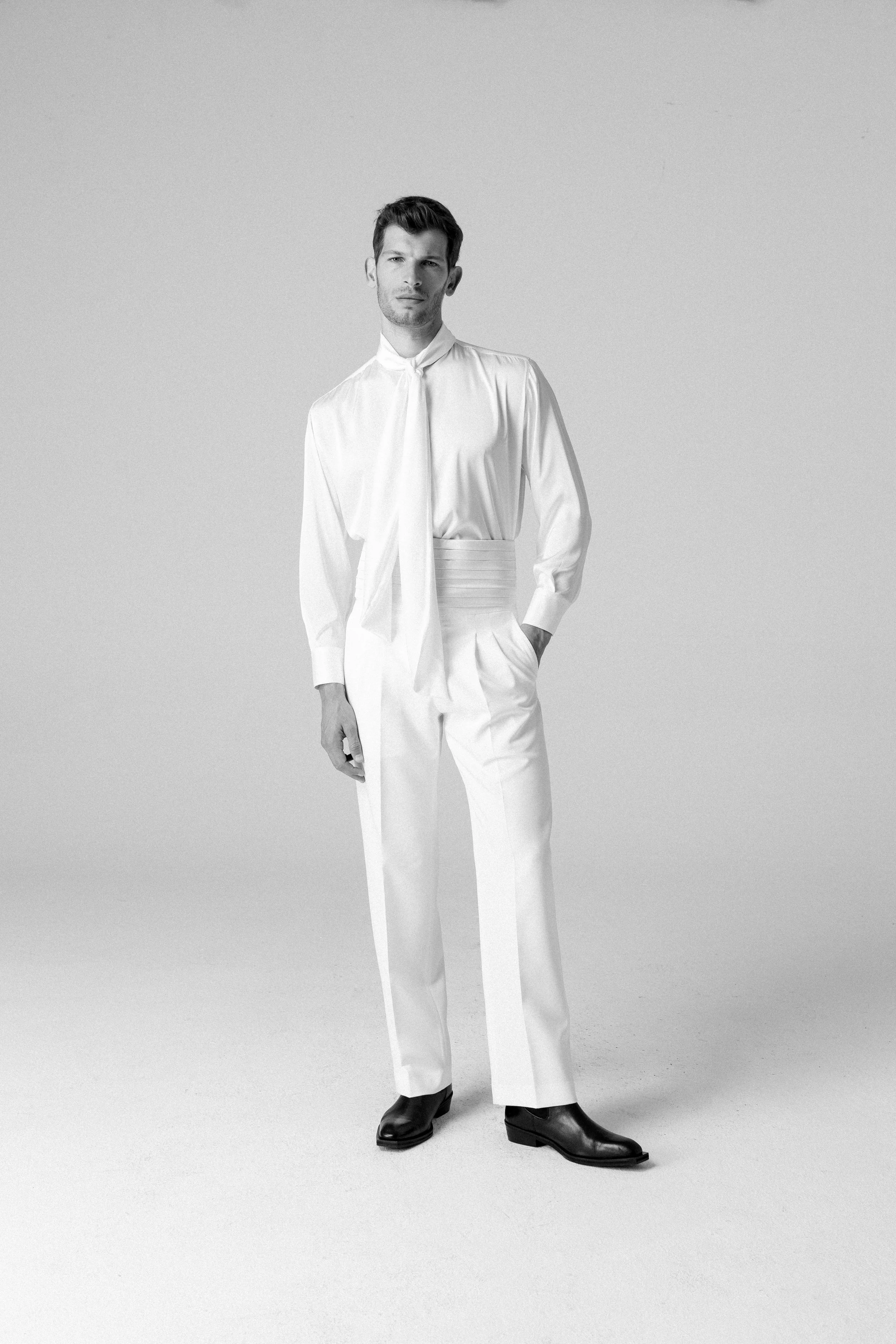 Uomo in abbigliamento elegante bianco, posa su uno sfondo neutro, in stile moda.