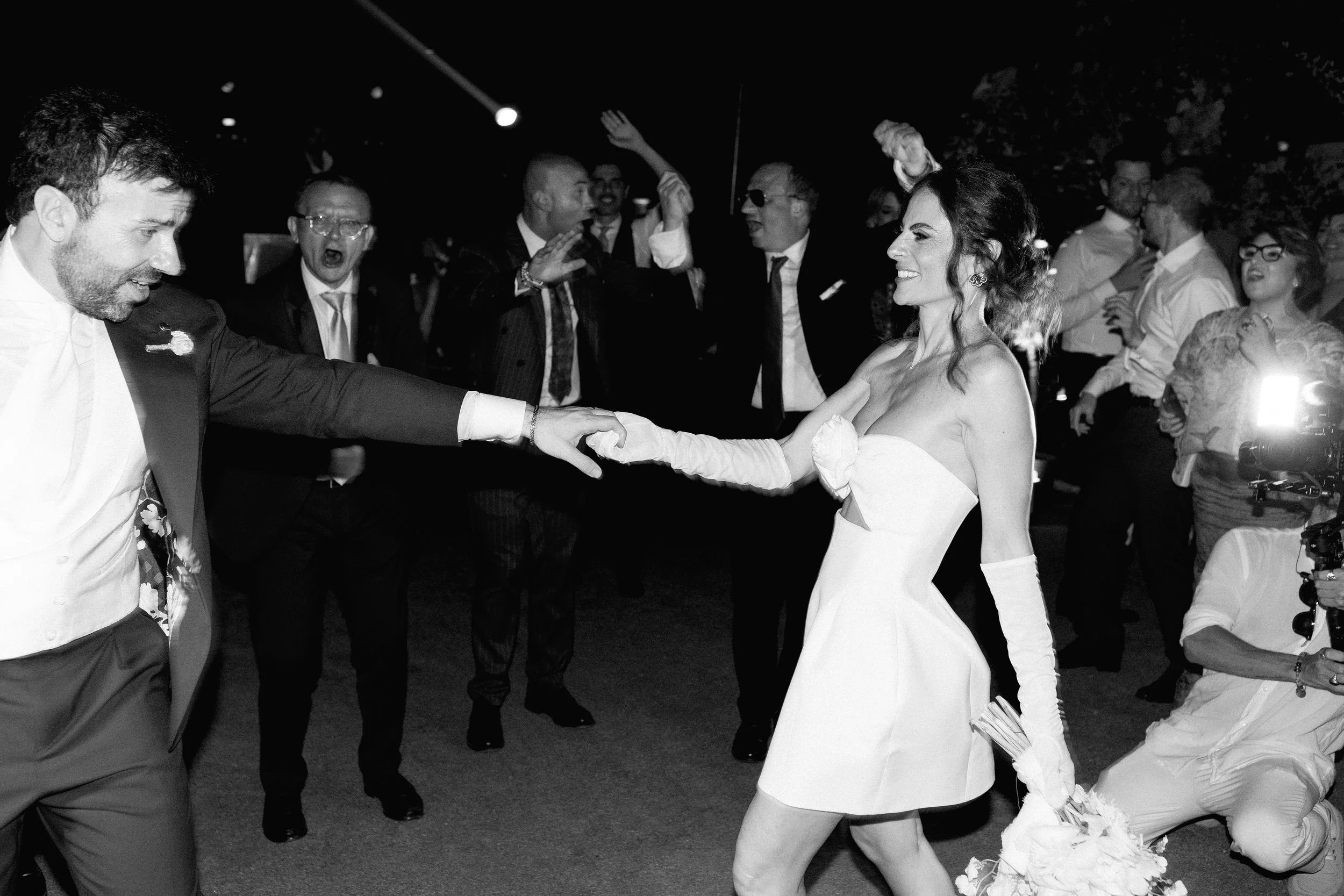 Sposi che ballano con amici in festa all'aperto di notte.