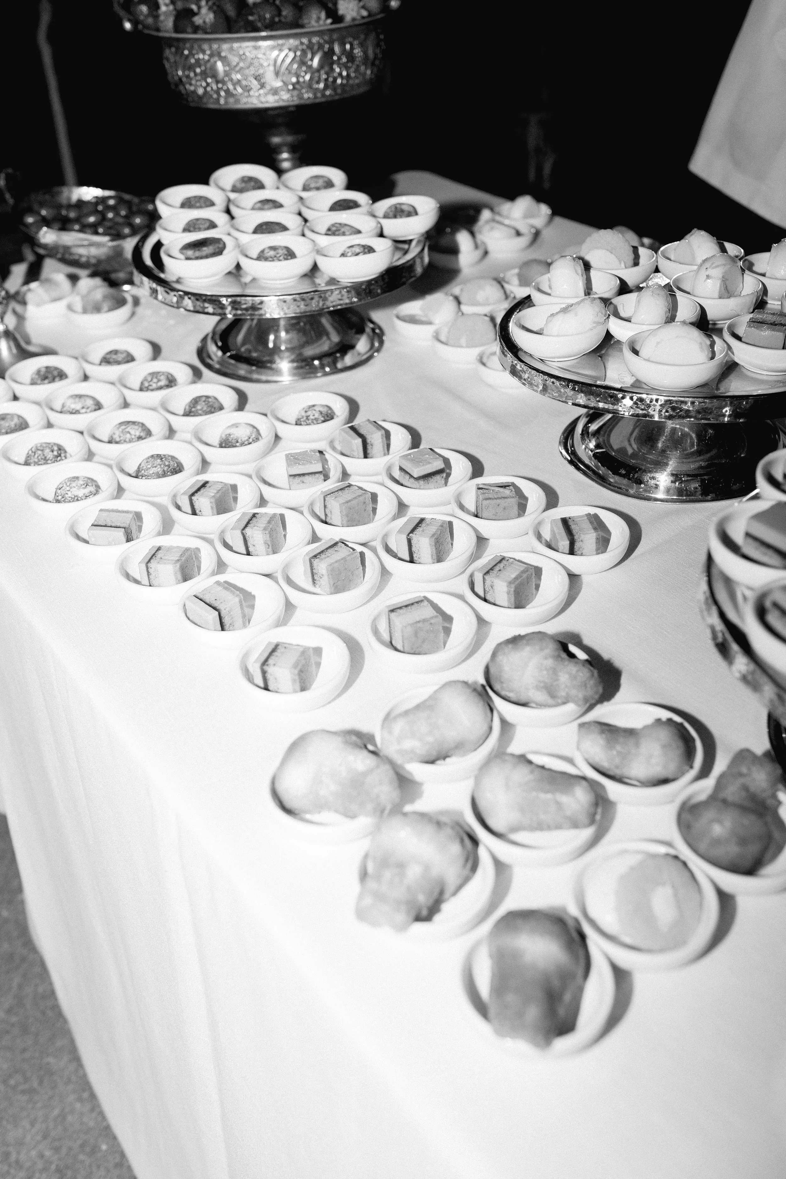 Tavolo con dolci e desserts serviti in ciotole e piatti di vari tipi, su basi di metallo.