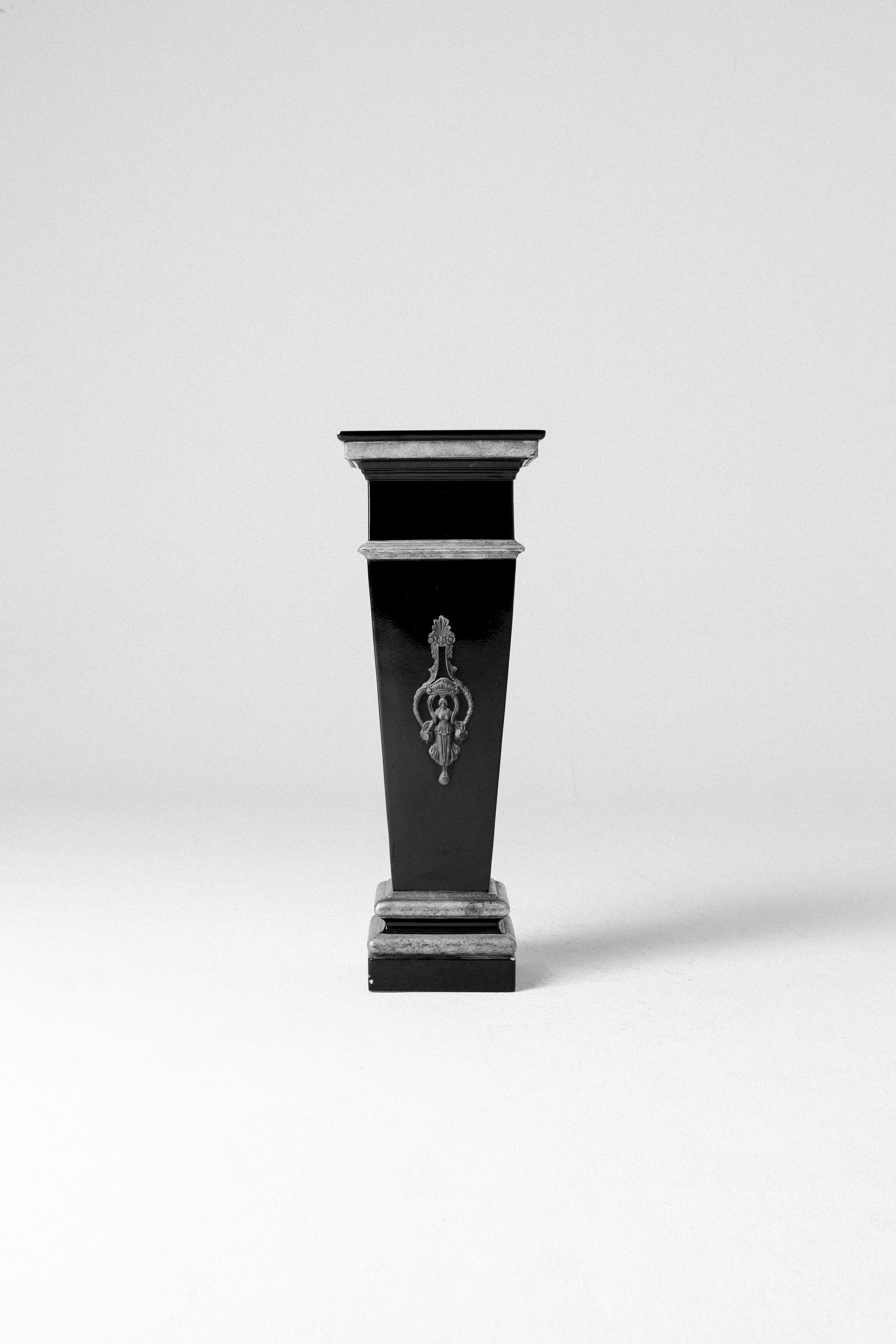 Colonnina in legno decorata con fregi e un medaglione centrale, posizionata su uno sfondo bianco