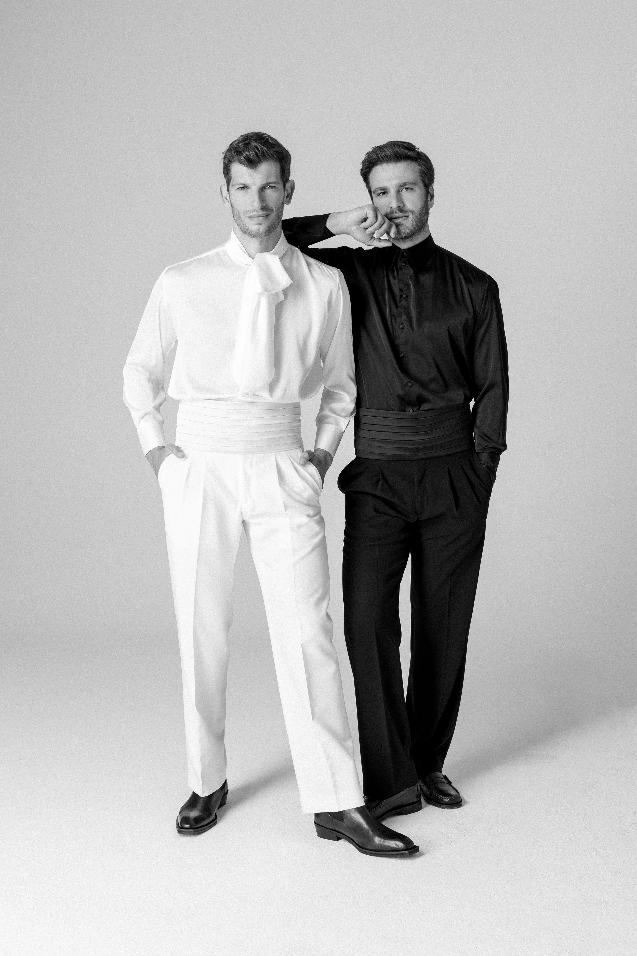 Due uomini vestiti formalmente, uno in bianco e uno in nero, in posa in studio.