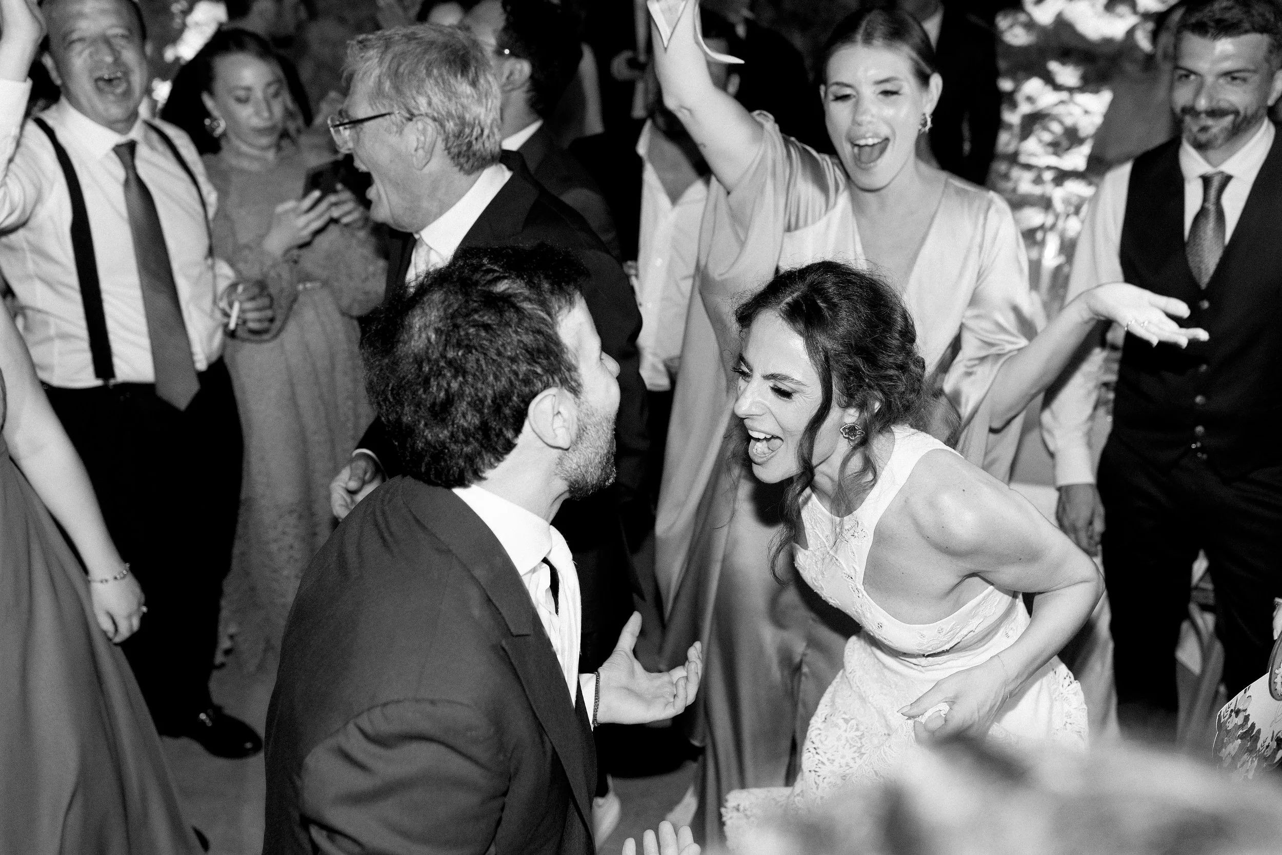 Persone che ballano e si divertono a una festa, alcuni sorridono e si abbracciano, in un ambiente festoso.