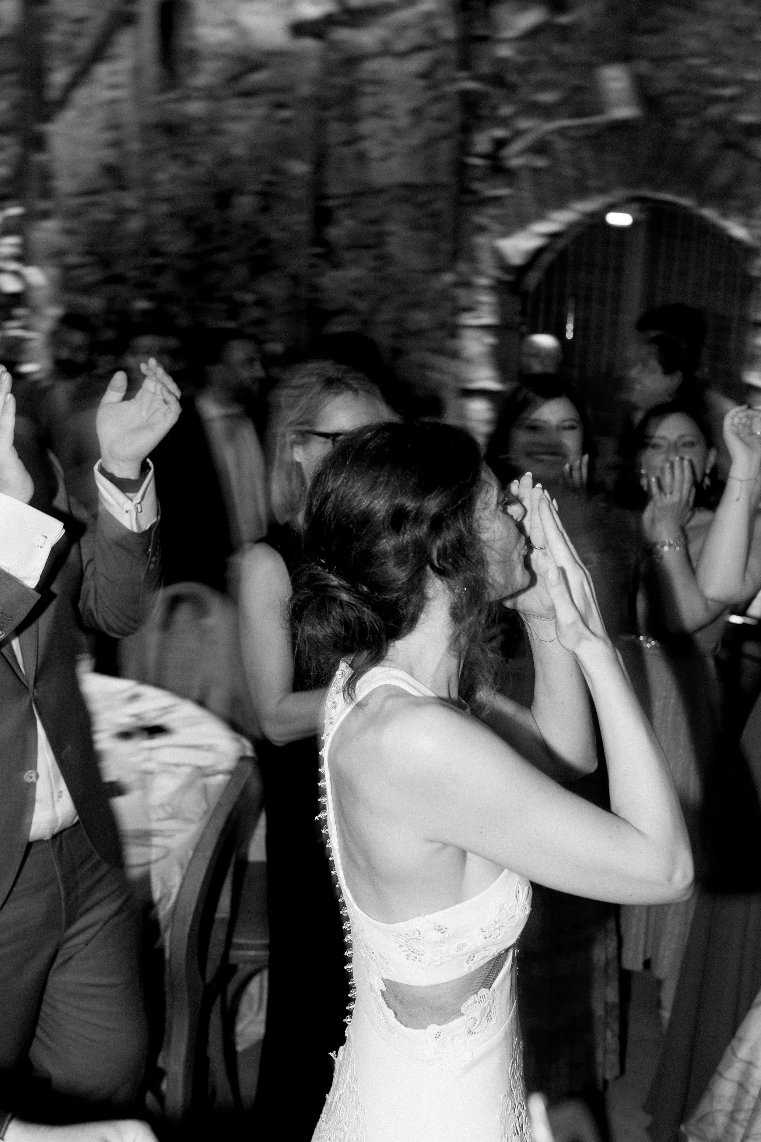 Un gruppo di persone a una celebrazione, con alcune che ridono e una donna in primo piano che pare star piangendo, in abiti eleganti.