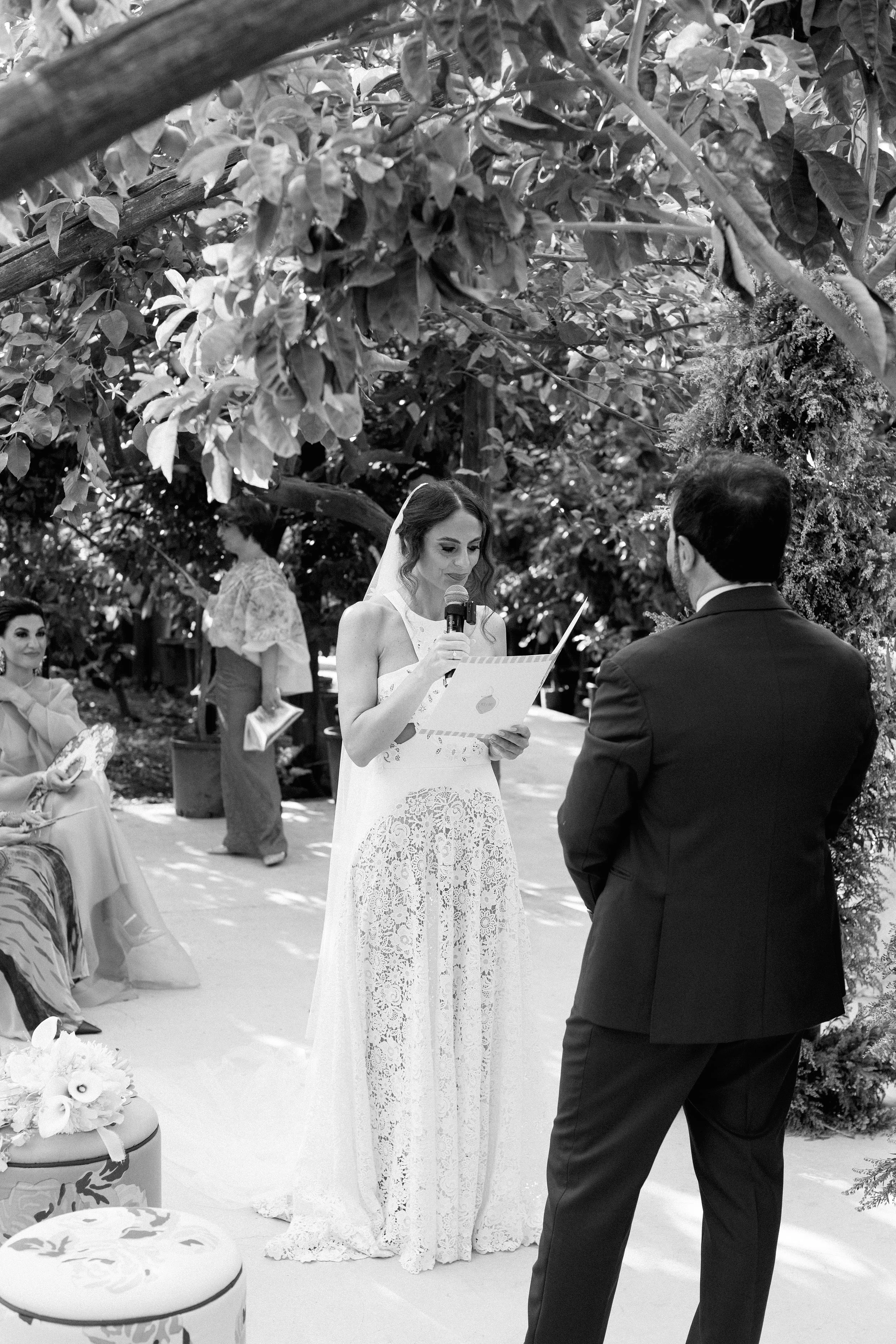 Una donna che legge i voti di nozze durante una cerimonia matrimoniale in un giardino.