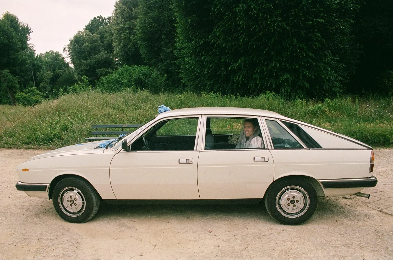 Auto d'epoca bianca parcheggiata su una strada sterrata con un cielo coperto, sullo sfondo alberi verdi e cespugli.