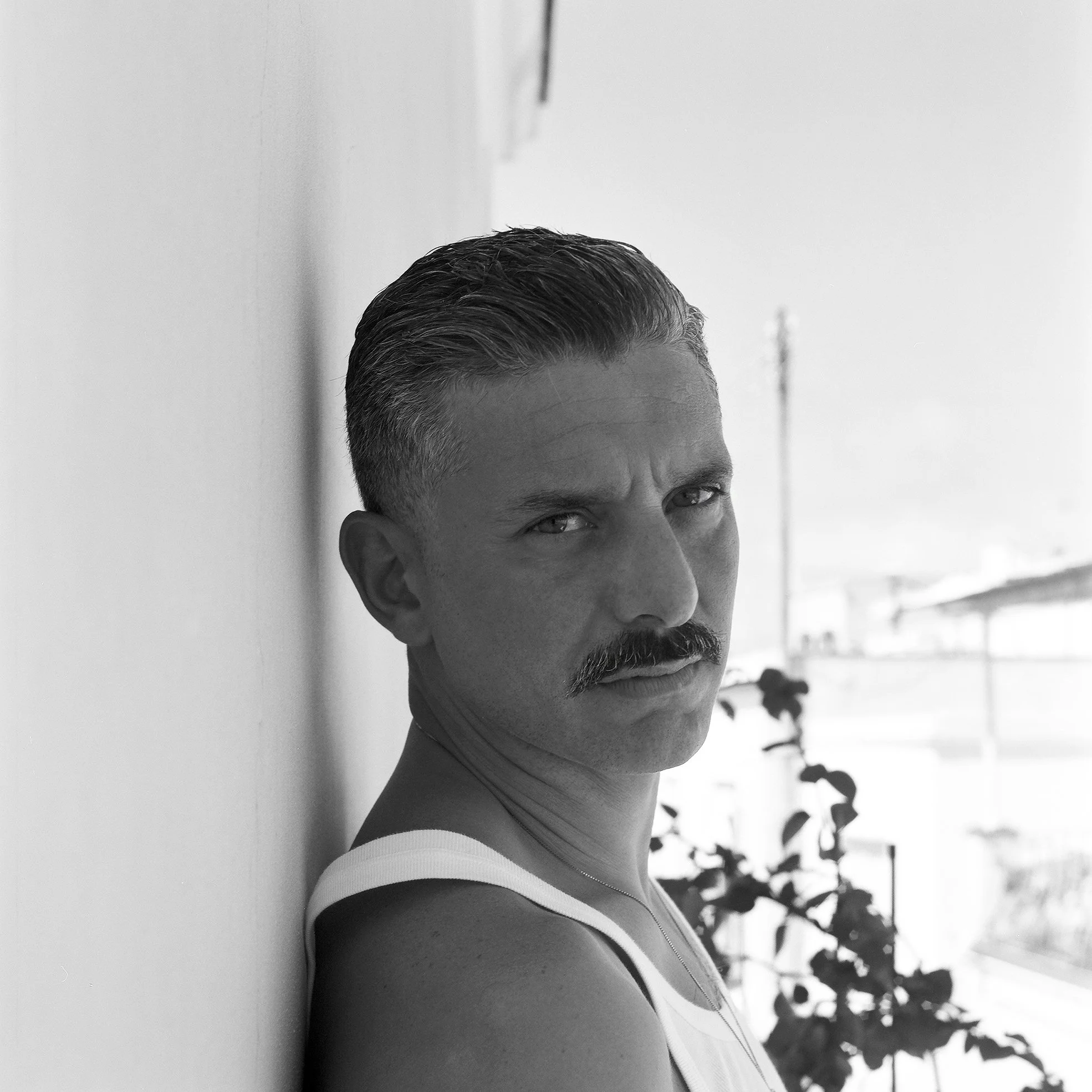 Ragazzo con baffi che si appoggia a una parete in un'immagine in bianco e nero, con sfondo di una finestra