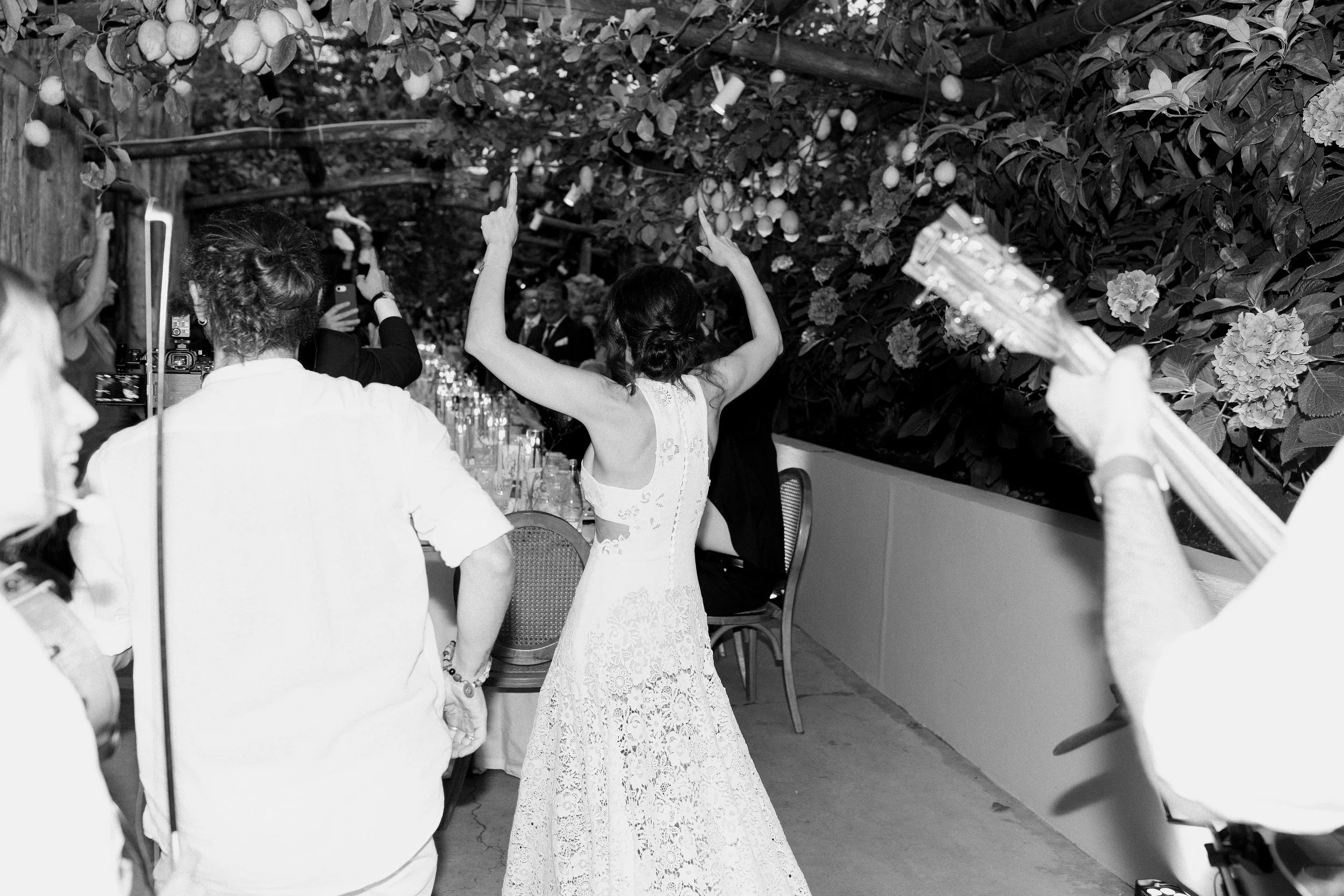 Una donna in abito da sposa balla tra gli ospiti durante un matrimonio, in un ambiente decorato con piante e fiori.