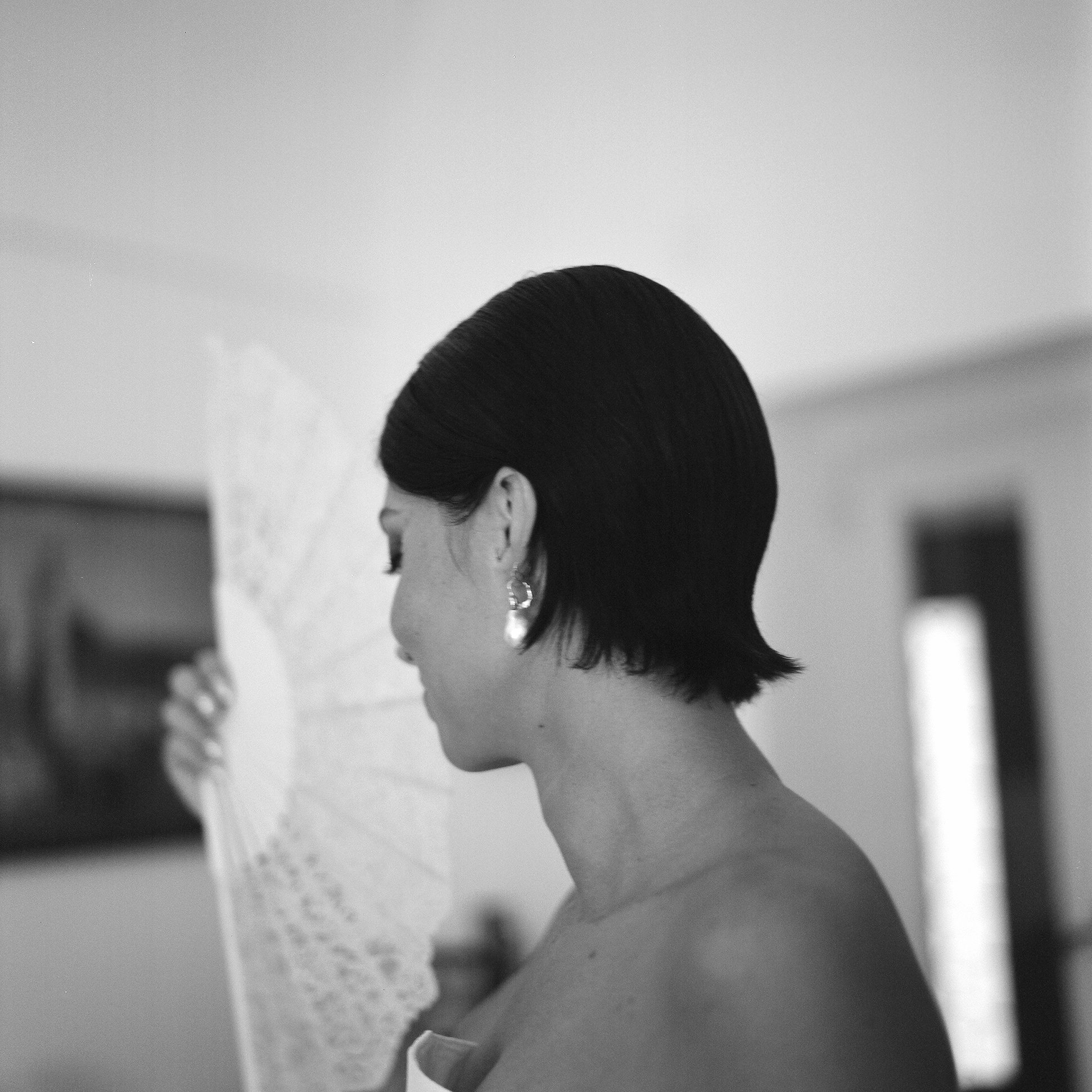 Donna con capelli corti neri e orecchini eleganti, con un cappello di paglia in mano, in un ambiente domestico.