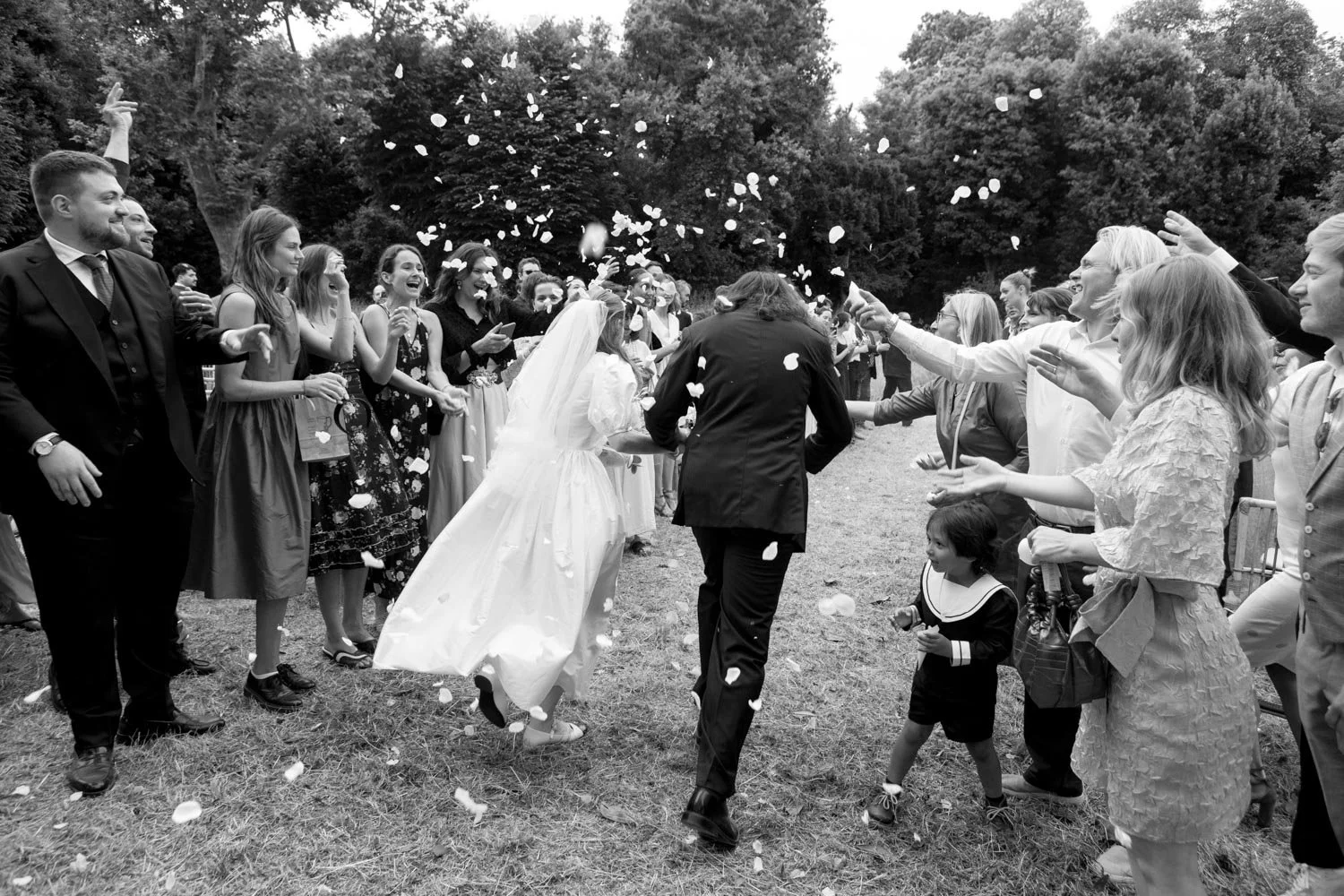 Una coppia di sposi che si bacia circondata da amici e parenti durante una celebrazione all'aperto, mentre lanciano petali di fiori.