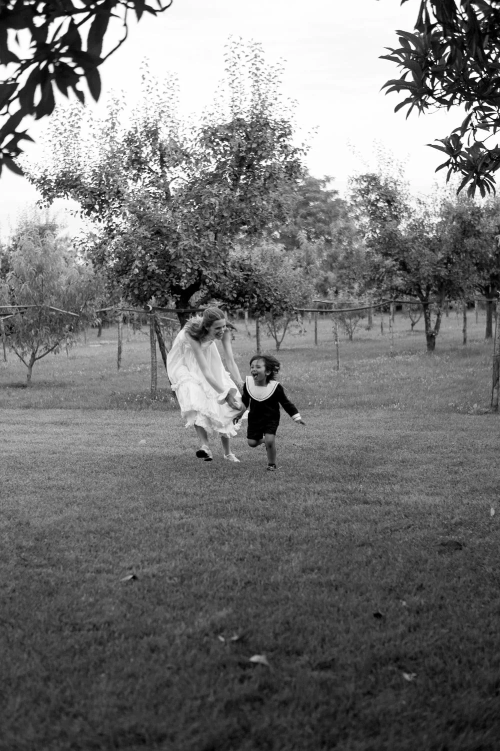 Due bambini che corrono e ridono nel parco, con alberi sullo sfondo in un'immagine in bianco e nero.