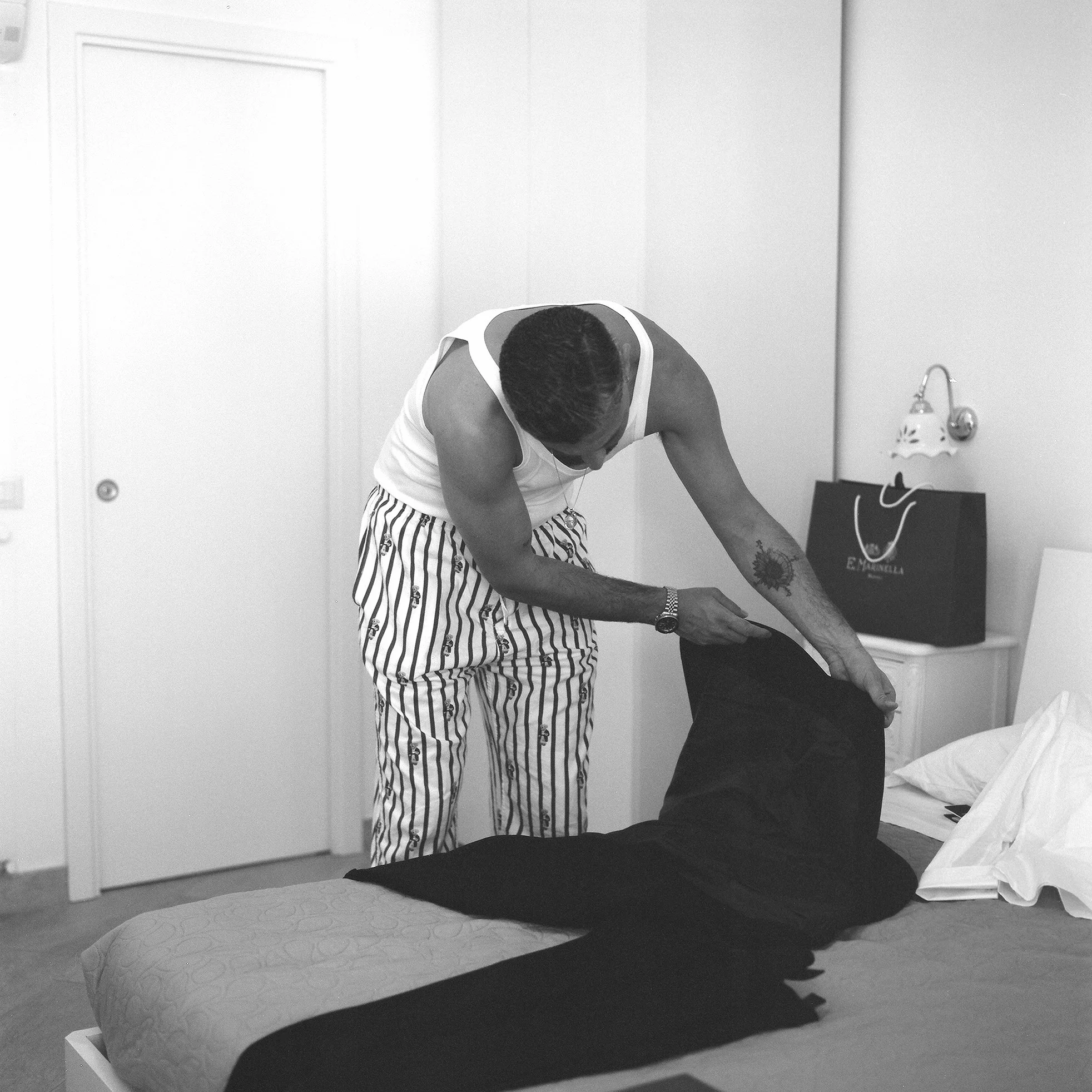 Un uomo in pigiama a righe aiuta una donna distesa sul letto a mettere un paio di pantaloni neri.