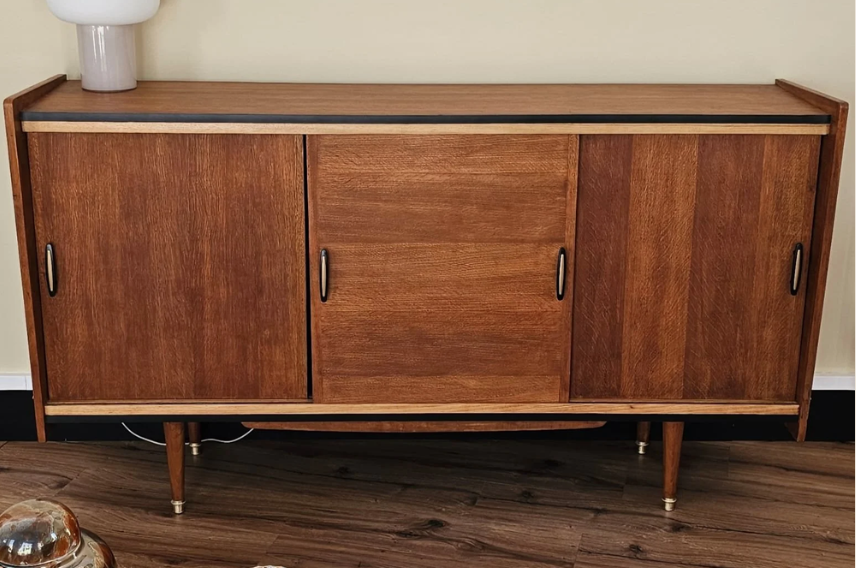 Buffet en bois avec portes coulissantes et quatre pattes, placé contre un mur beige.