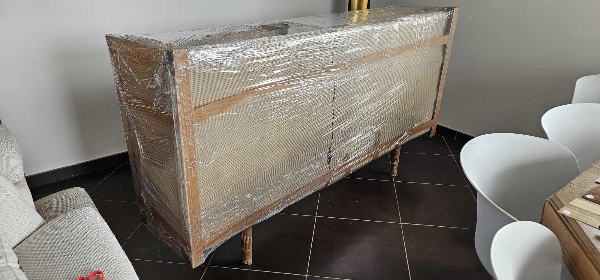 Armoire en bois partiellement recouverte de plastique transparent, située dans une pièce avec des murs clairs et un sol carrelé noir.