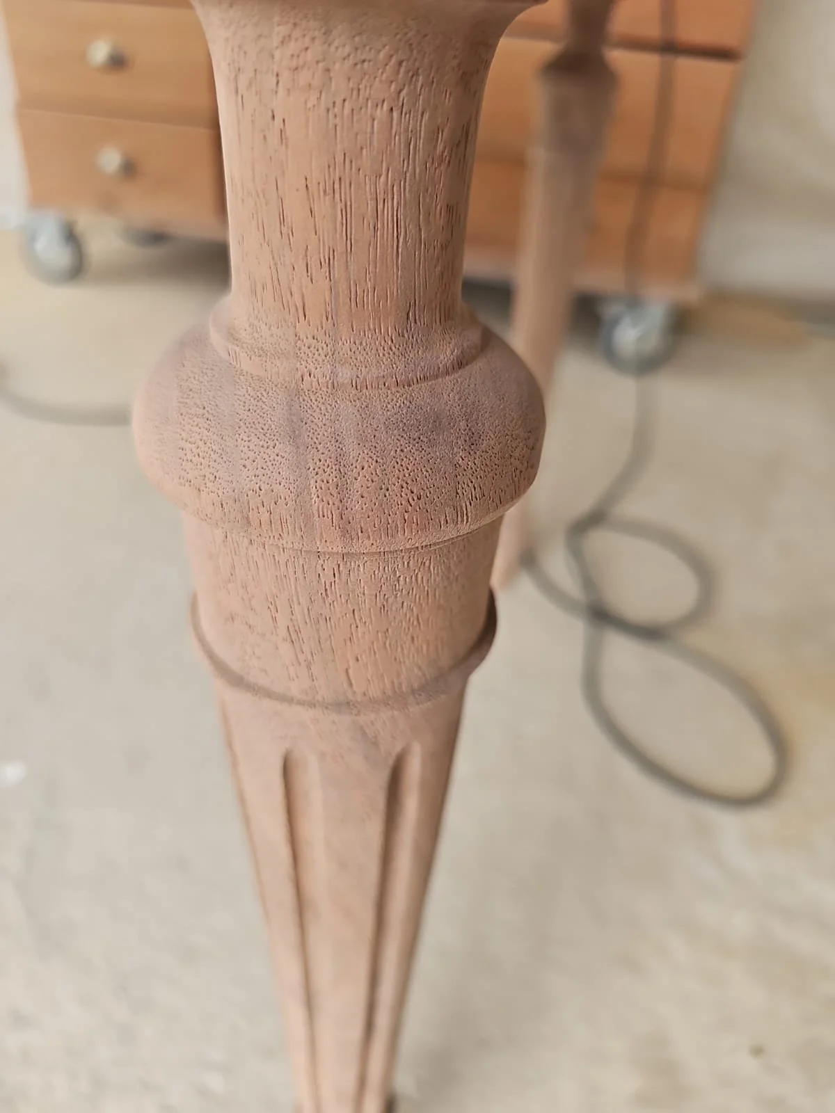 Détail d'une pièce en bois, probablement la jambe d'une table ou d'un meuble, avec une finition lisse et structurée.