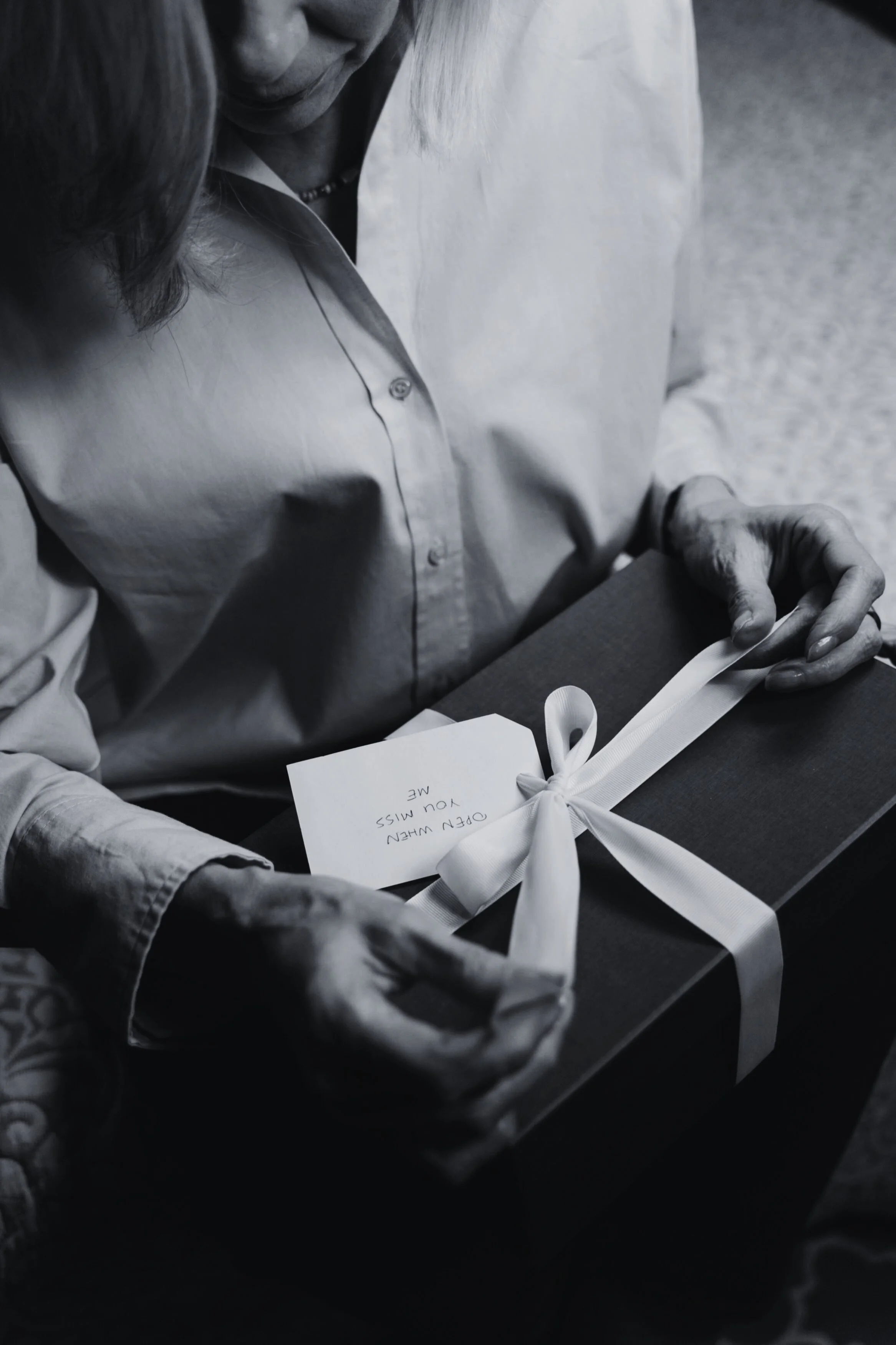 A person holding a gift wrapped with a white ribbon and a note that says, 'Open when you miss me.'
