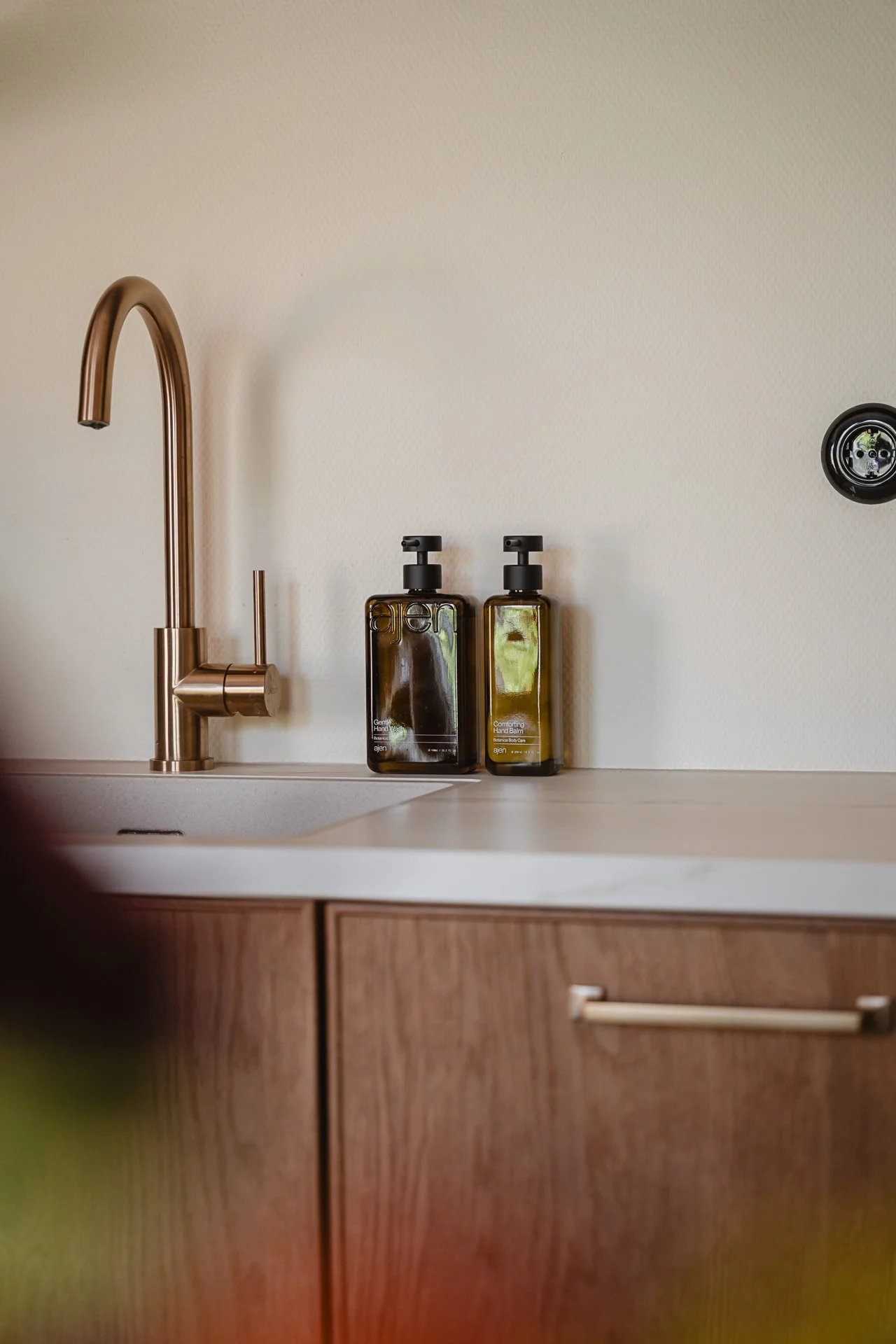 Een keukenspoelbak met een stijlvolle koperen waterkraan en twee amberkleurige dispensers met zeep.