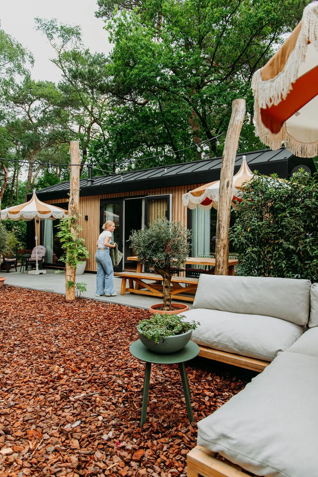 Een tuin met een tiny house, buitenmeubilair en parasols van Karwei. Rondom groene bomen.