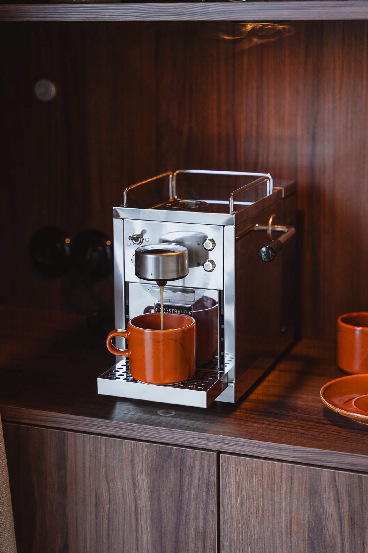 Een espressoautomaat die koffie schenkt in een oranje kop op een houten keukenblad.