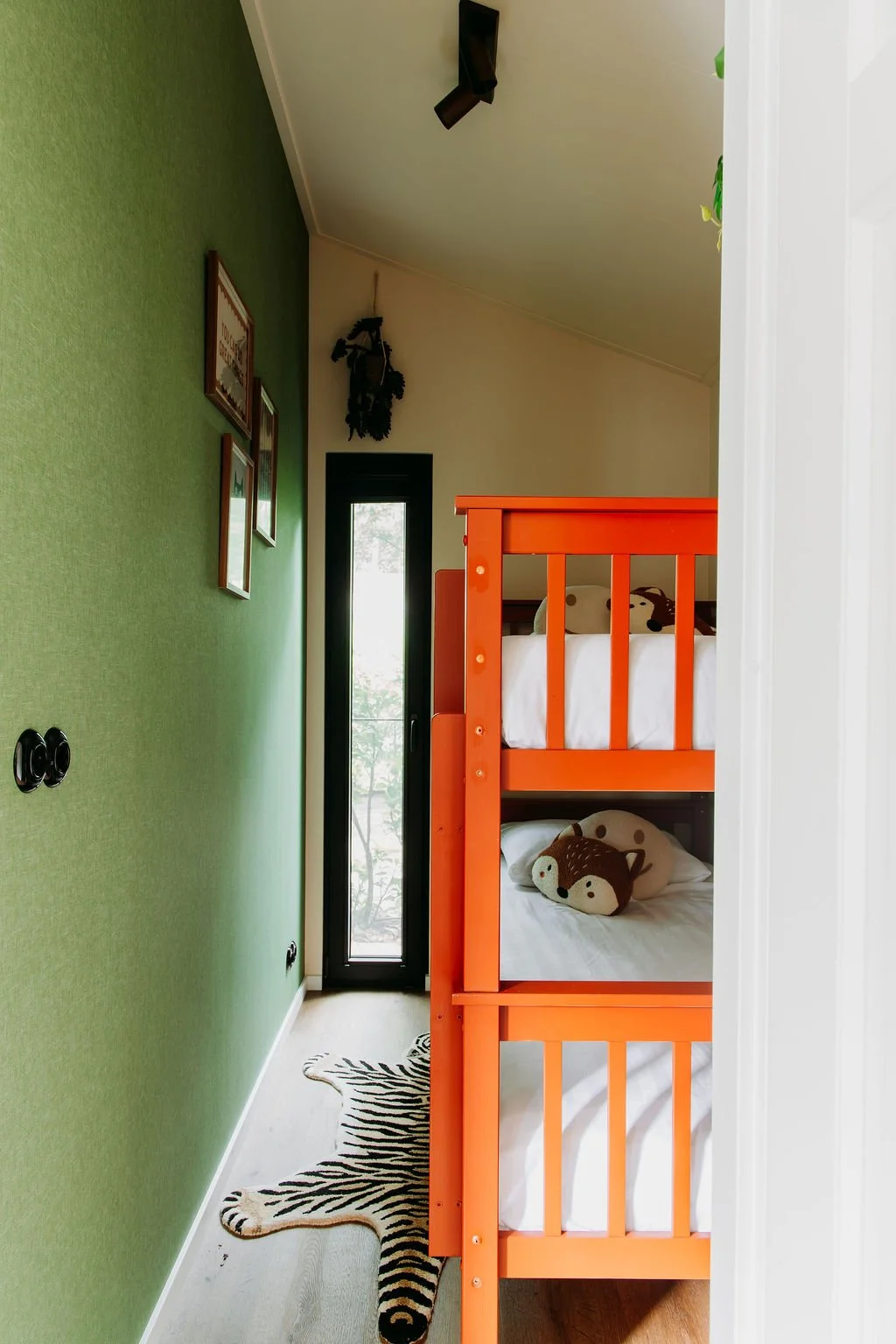 Een kinderkamer met een groene muur, een kast met drie foto's aan de muur en een stapelbed met een oranje frame en knuffelberen op de bedden.