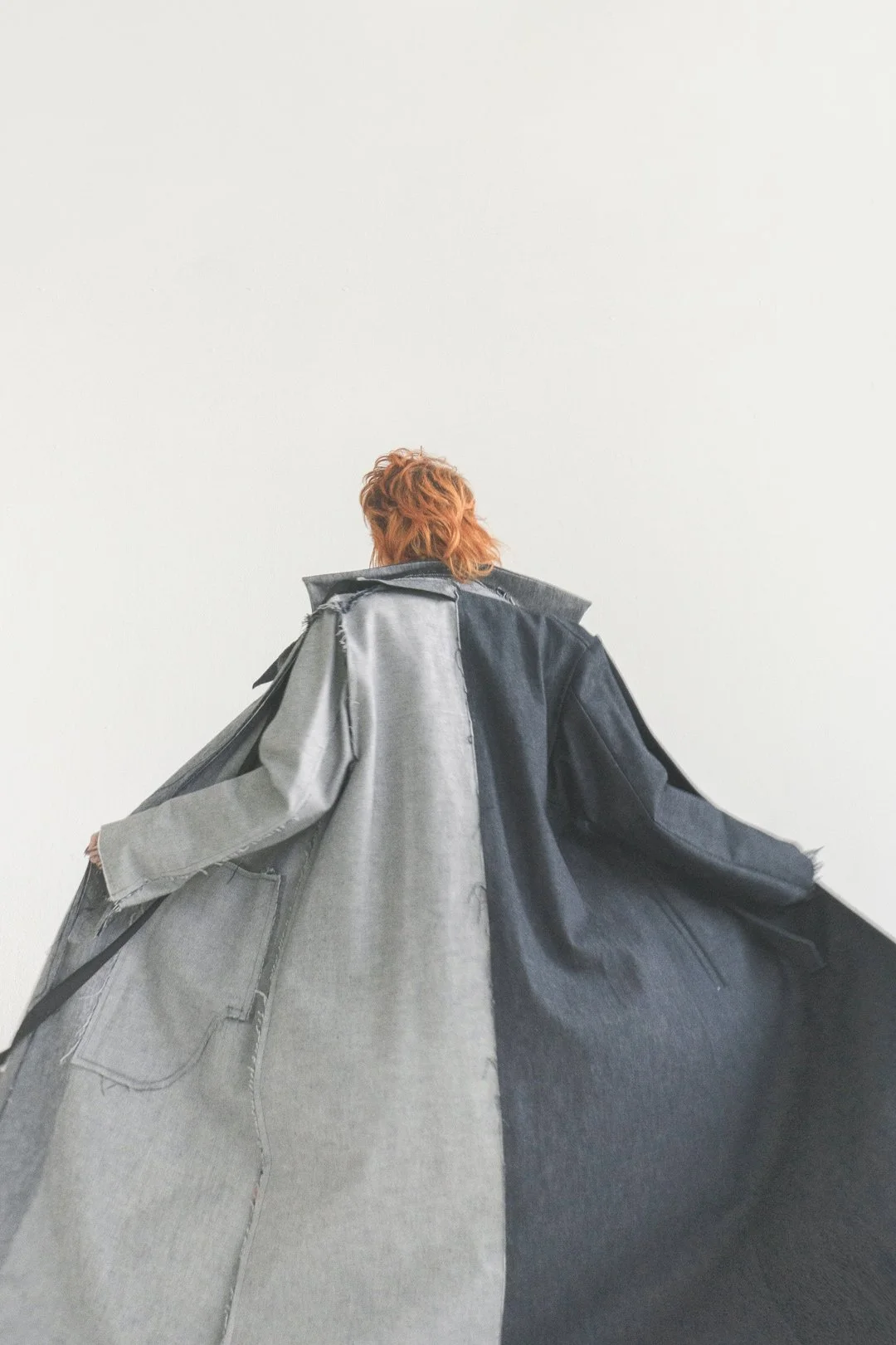 Rückenansicht Person trägt einen Jeansmantel von Julia Schürmann - raum6.7 und breitet die Arme aus sodass dieser breitflächig zu sehen ist.
