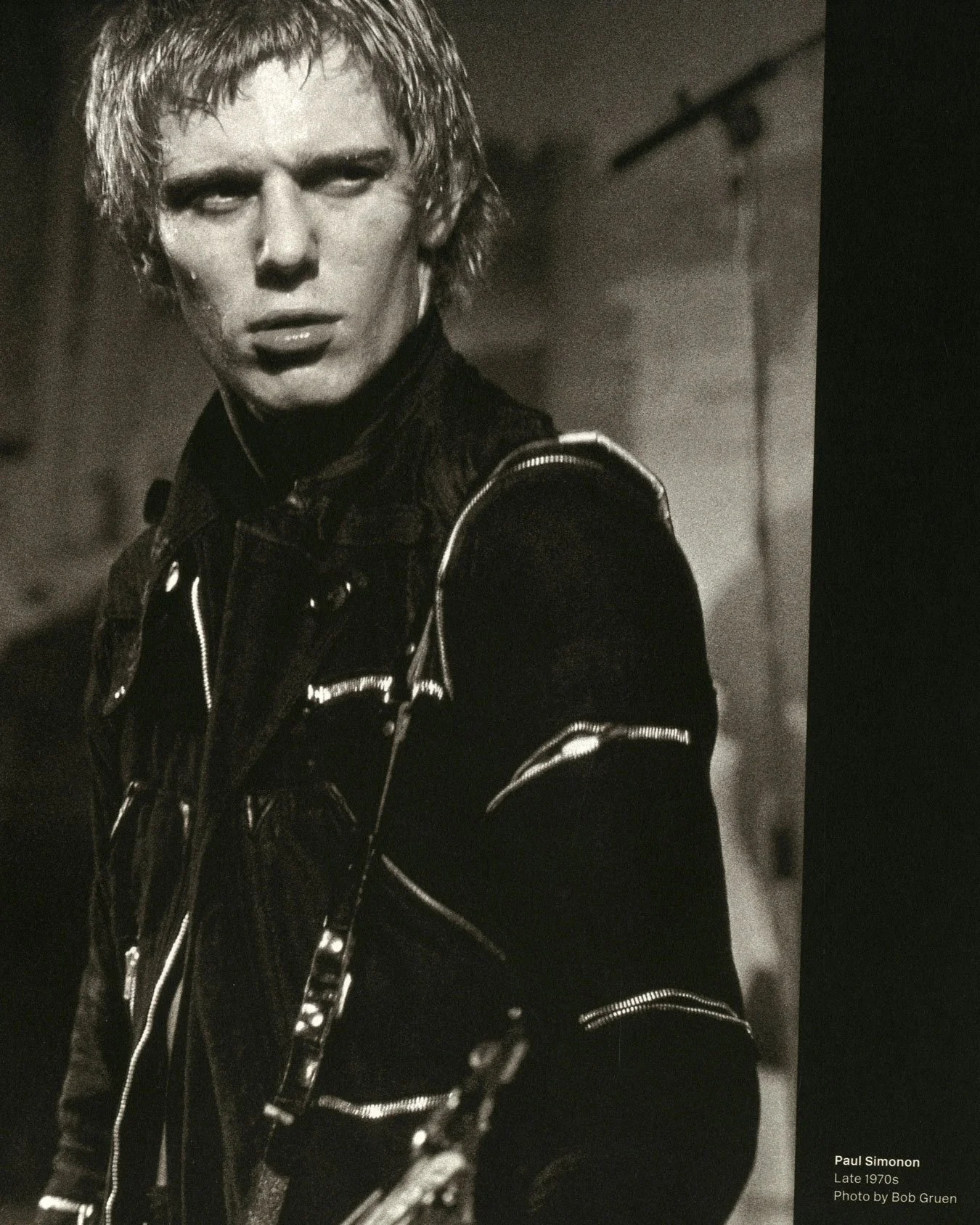 Schwarz-Weiß-Foto eines jungen Mannes mit wilder Frisur in Lederjacke mit vielen Reißverschlüssen, aufgenommen in den späten 1970ern.