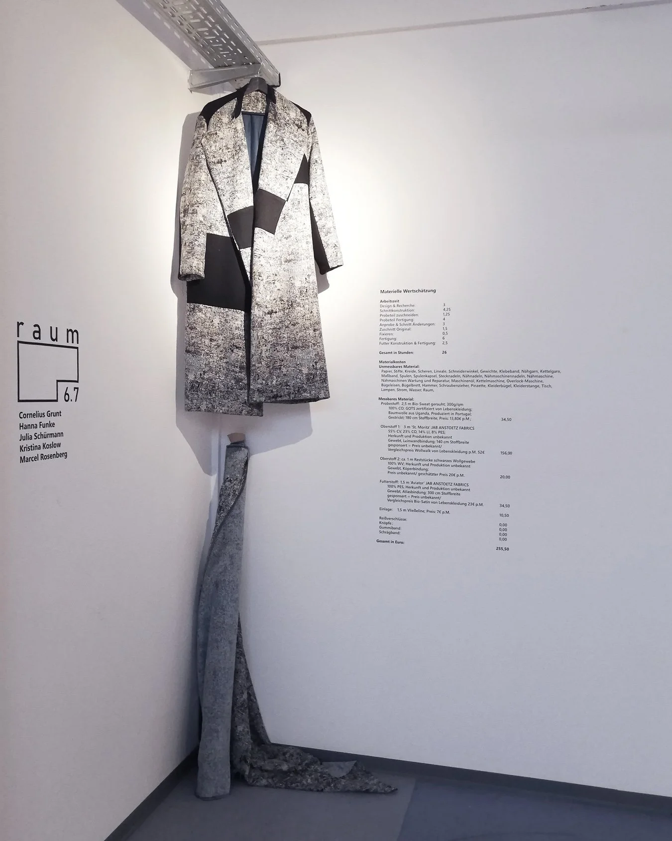 Ausstellungskompositzion aus: Mantel, Stoffrolle, Text, Logo mit aussteller*innen Infos