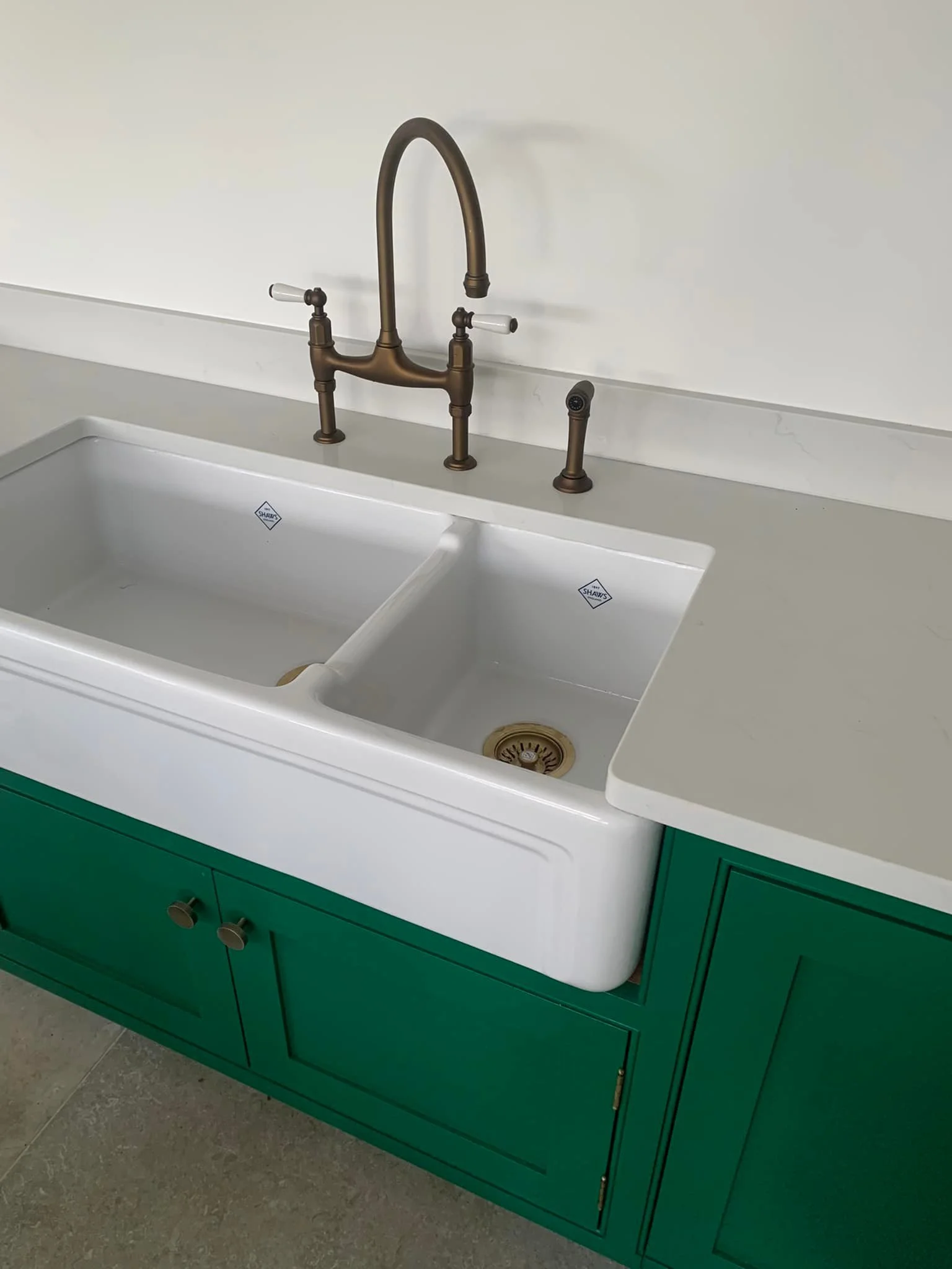 White farmhouse-style kitchen sink with two basins, brass faucet, and green cabinet.