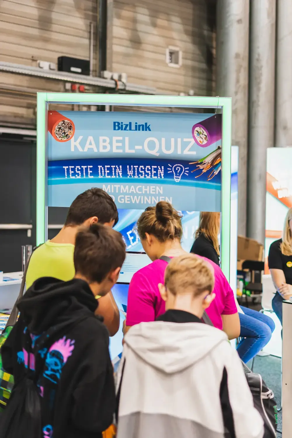 Menschen, die an einem Kabel-Quiz bei einer Messe teilnehmen, mit einem Bildschirm, auf dem die Fragen angezeigt werden.