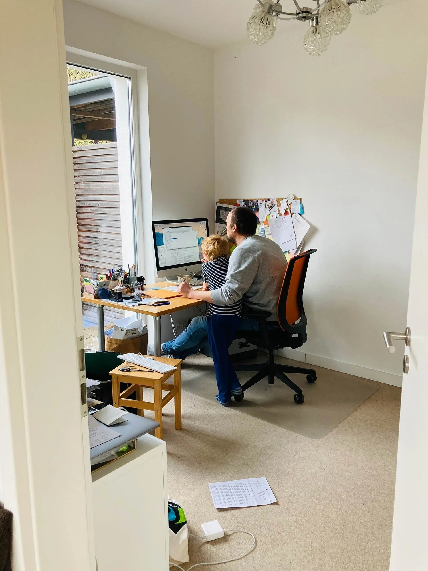Größeres Bild von Superidee Chef Ulf im Home Office an seinem Arbeitsplatz mit einem kleinen Kind auf dem Schoß. Zusammen schauen sie auf den Monitor eines Computers. Um sie herum sind Arbeitsmaterialien.