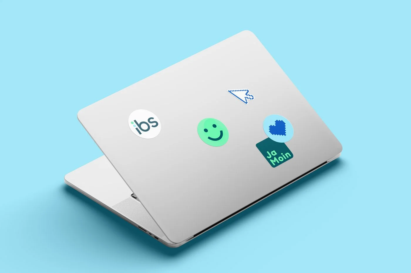 Ein Laptop mit Aufklebern, darunter ein IGS-Logo, ein lachendes Gesicht, ein Pfeil, ein Herz und ein 'Ja Main'-Sticker, auf hellblauem Hintergrund.