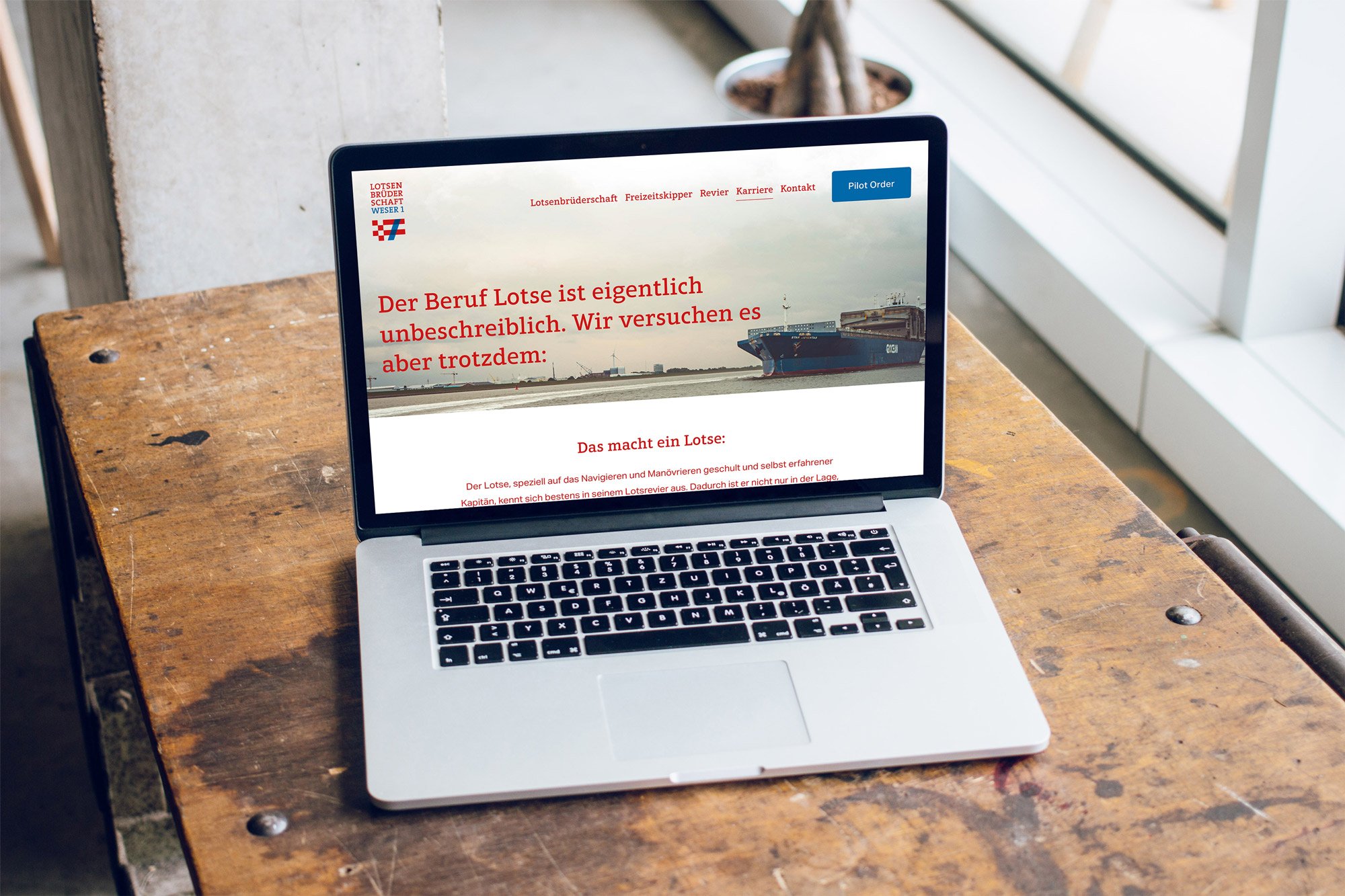 Laptop auf einem alten Holztisch, der eine Webseite über die Berufssparte Lotse zeigt. Das Bild stammt aus einem modernen Raum mit großen Fenstern.