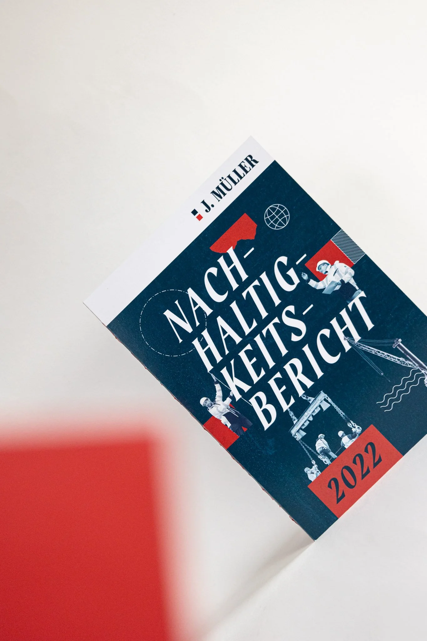 Buchcover mit dem Titel 'Nachhaltigkeit, Hauss, Technik, Berichte' und dem Jahr 2022, das oben rechts sichtbar ist. Das Buch hat eine dunkle blaue Farbgestaltung mit grafischen Elementen wie eine Weltkarte, Bauarbeiter, und technische Skizzen.