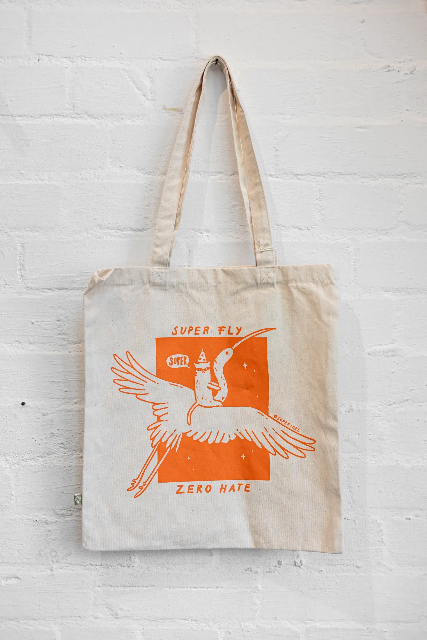Die Super-Tasche mit der Aufschrift "Super fly zero hate" hängt an einer weißen Ziegelmauer