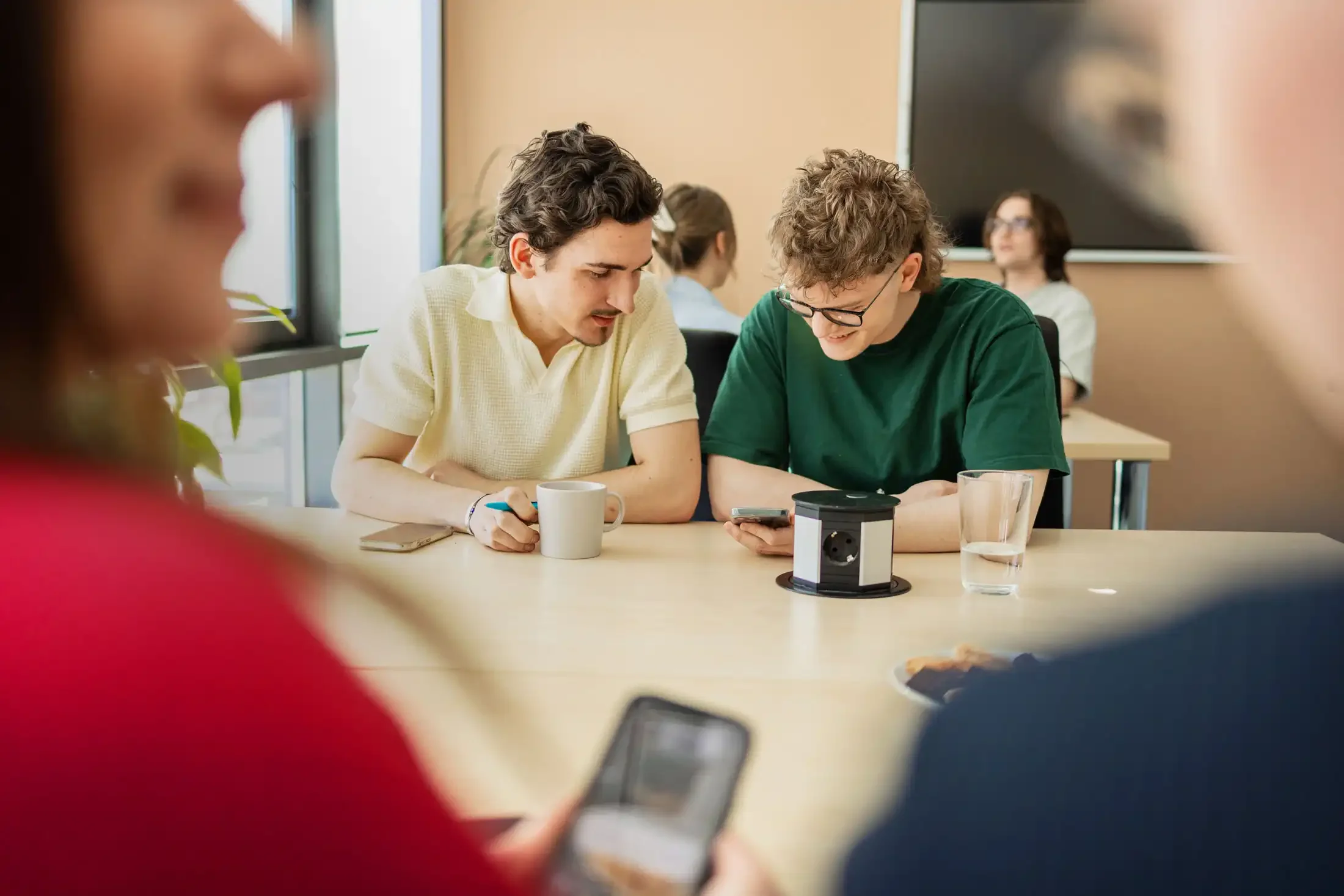 Zwei junge Studierende der IBS Oldenburg sitzen zusammen am Tisch und schauen gemeinsam auf ein Smartphone.