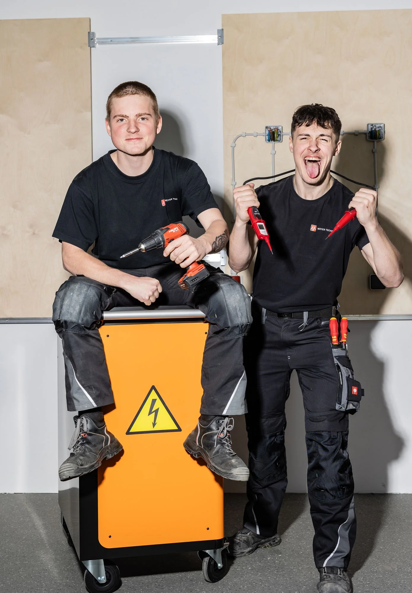 Zwei junge Männer mit Elektroniker Werkzeugen lachen in die Kamera.