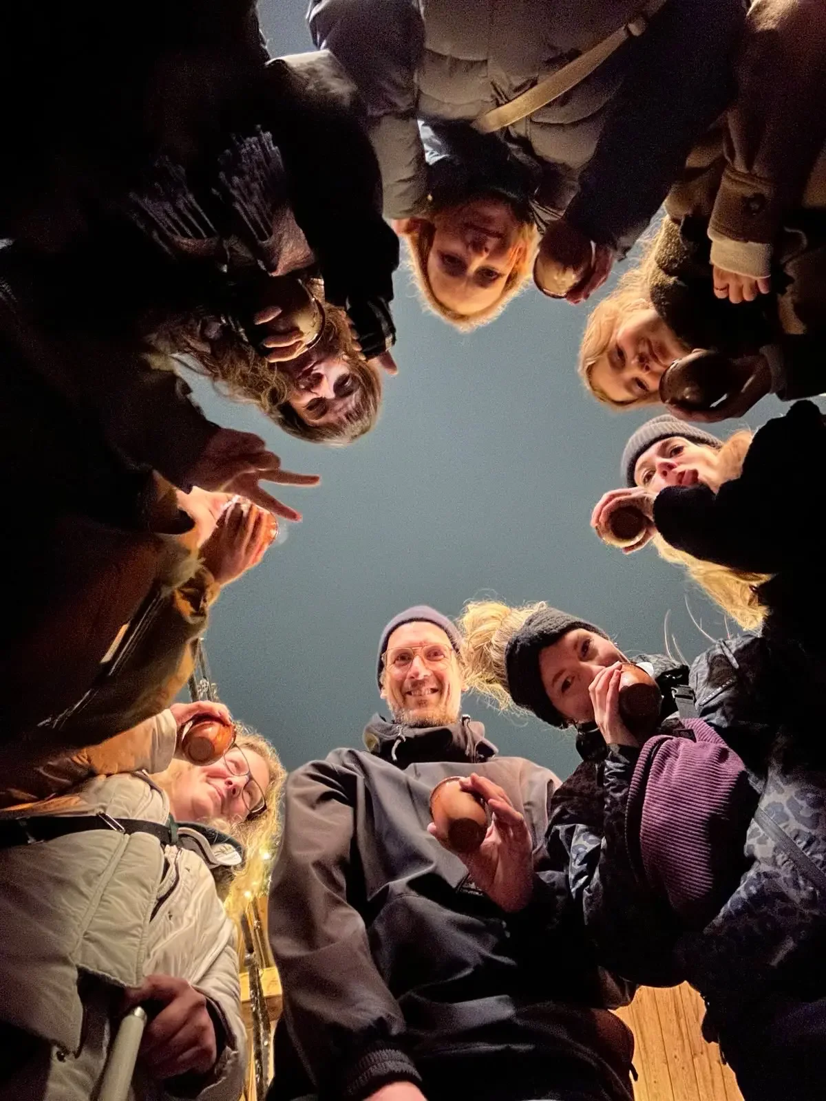 Gruppe von Menschen, die im Kreis unter einem dunklen Himmel stehen, einige halten Getränke und lachen.