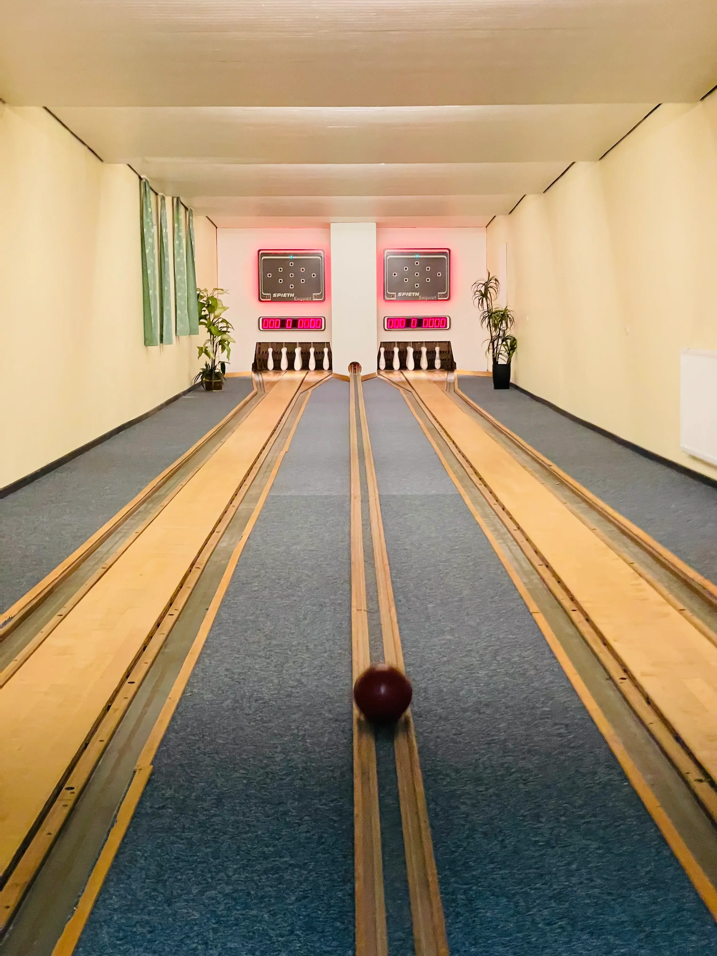 Ein Raum mit einer Ballspielbahn, auf der ein Billardkugel rollt. Im Hintergrund sind zwei elektronische Punktanzeigen und zwei Billardtische auf den Wänden.
