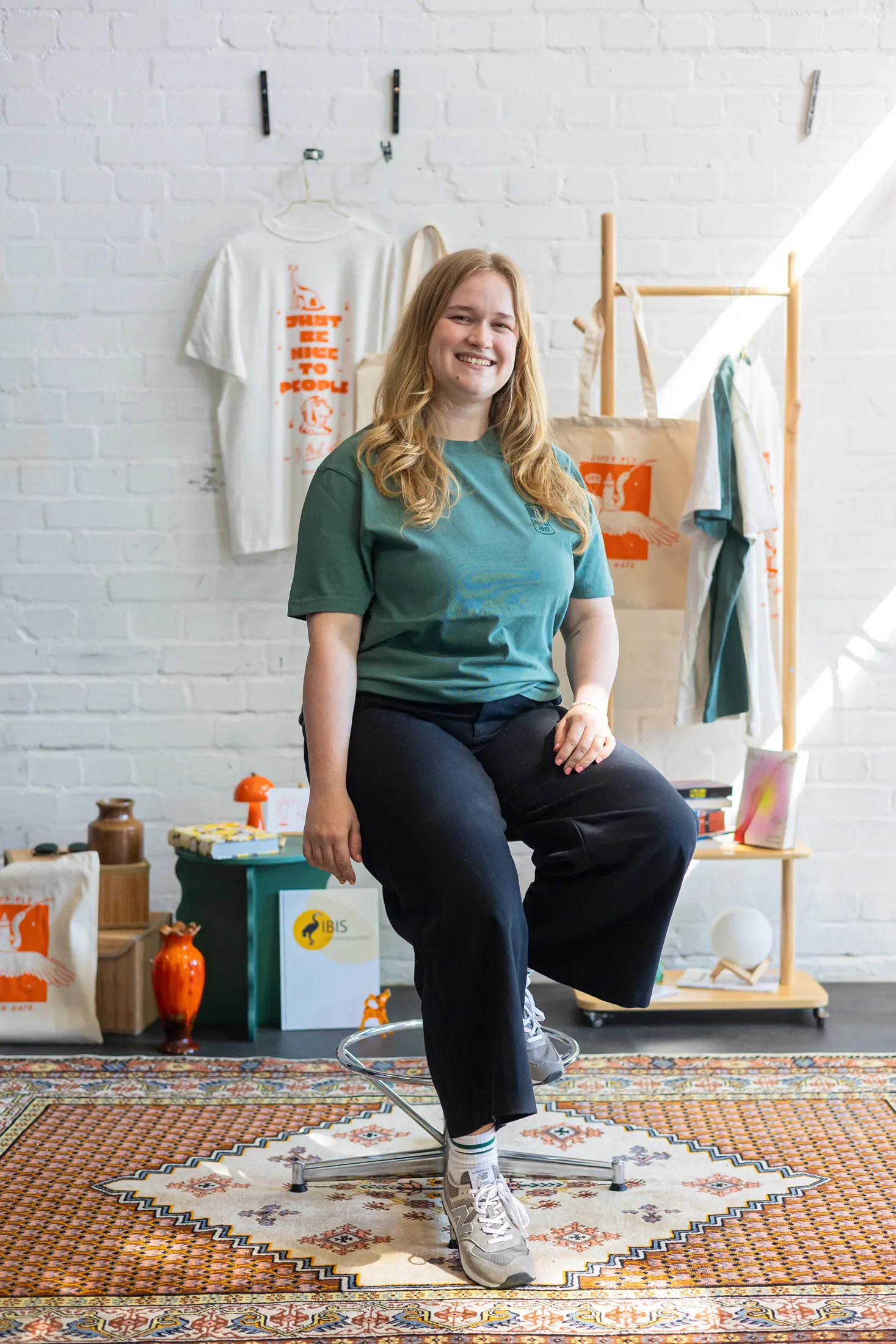 Eine Frau in grünem T-Shirt sitzt auf einem Hocker und lächelt in die Kamera.