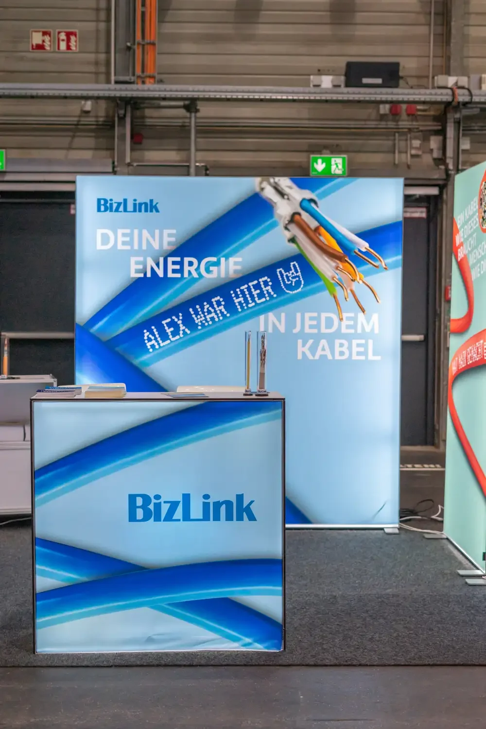 Messestand von BizLink mit der, die Kabeltechnik hervorhebenden, Slogan 'Deine Energie in jedem Kabel' und einem Kabel mit sichtbaren Kupferdrähten.
