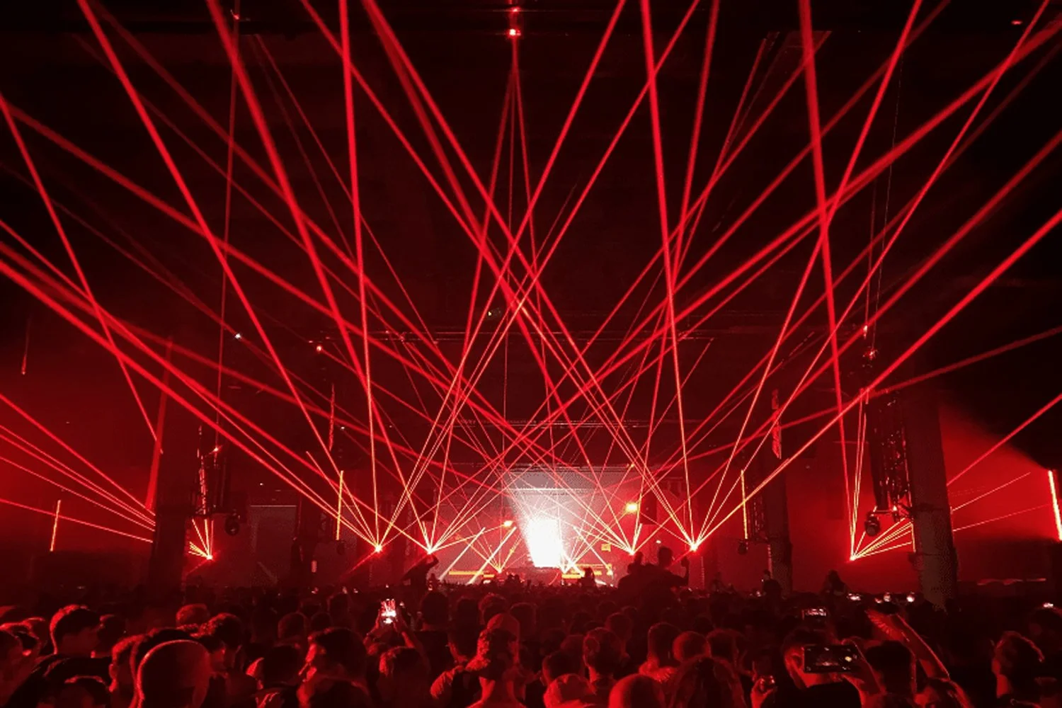 Concert scene with red laser lights crisscrossing above a crowd of people